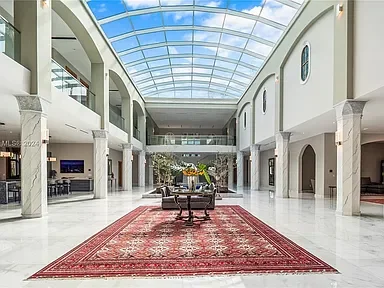 Interior of a spacious, modern building with a glass ceiling, white walls, and a red area rug with furniture on it.