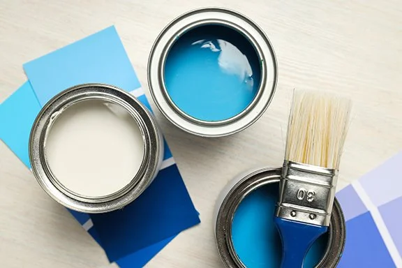 Open paint cans with blue and white paint, a paintbrush, and color swatches on a light surface.