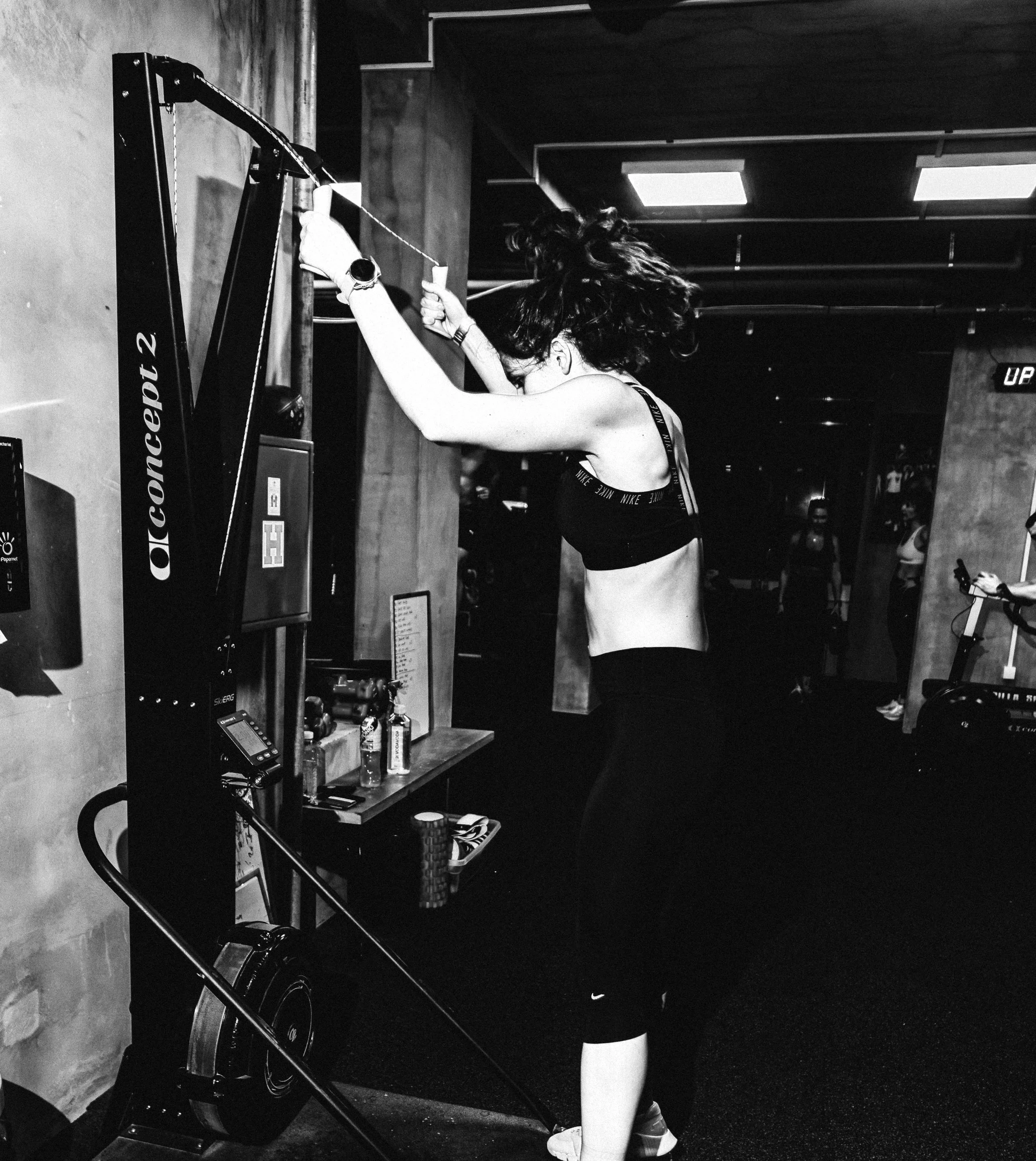 A woman in workout clothes is adjusting a cable machine in a gym.