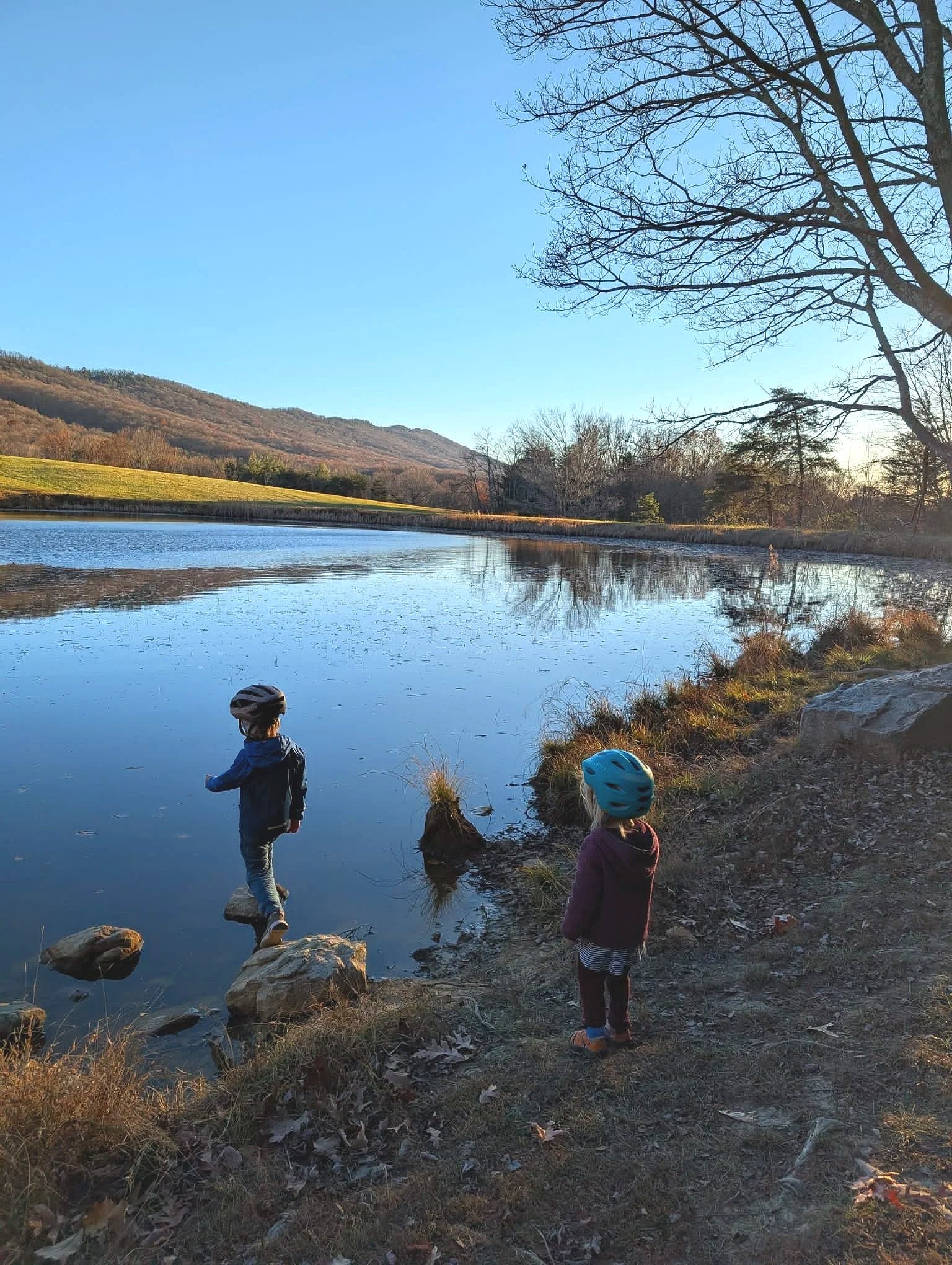 Two kids wearing helmets and playing at a calm lake on a Fall day