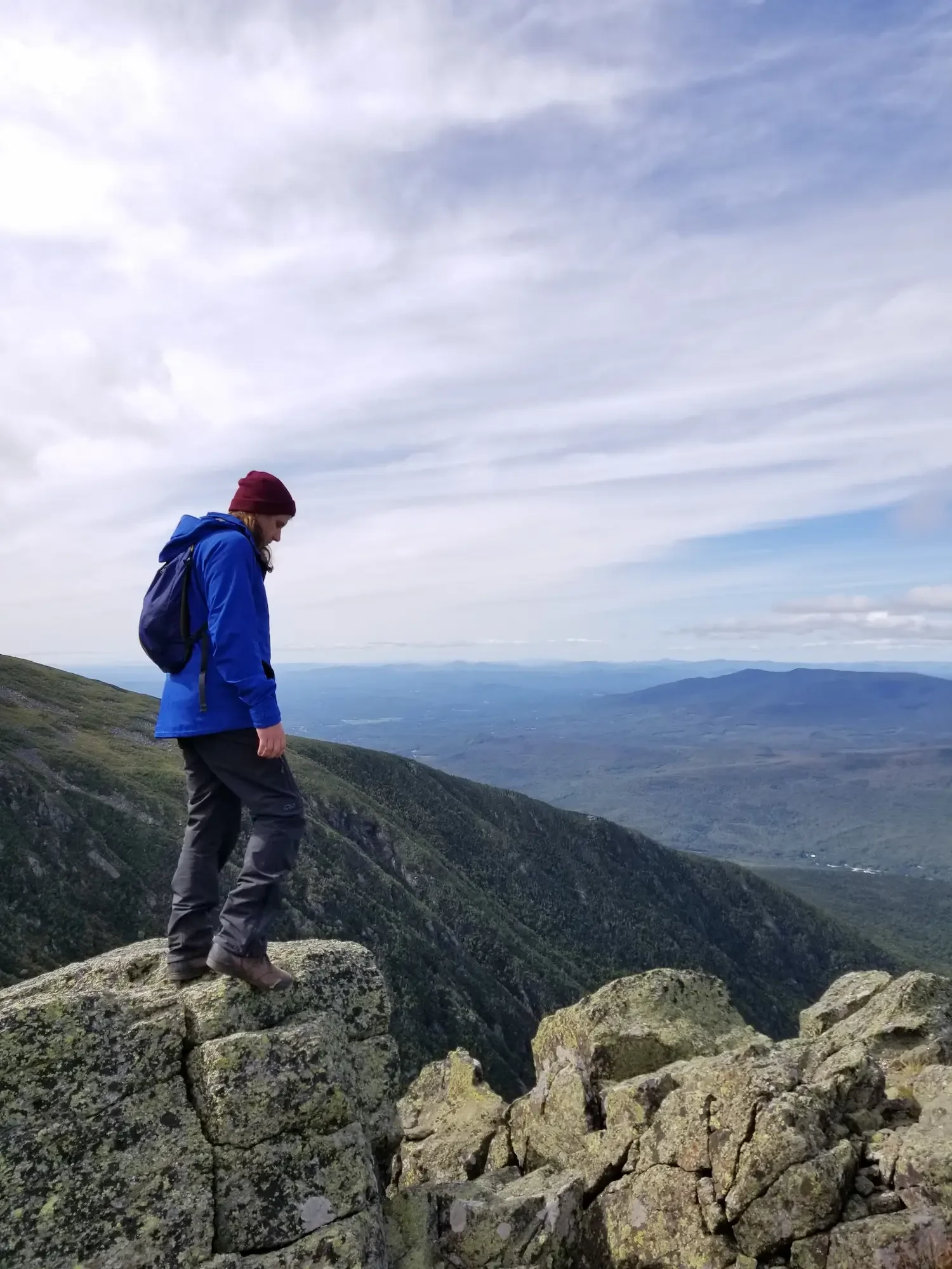 Man hiking over mountains wearing Outdoor Research pants, jacket, backpack and hat
