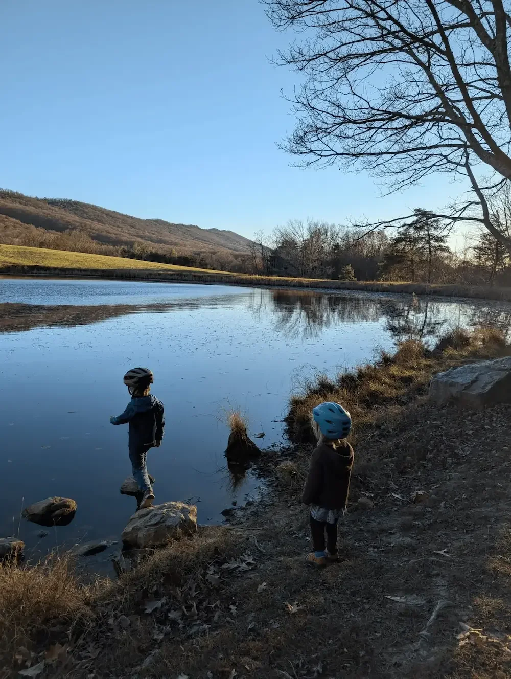 Two kids wearing helmets and playing at a calm lake on a Fall day