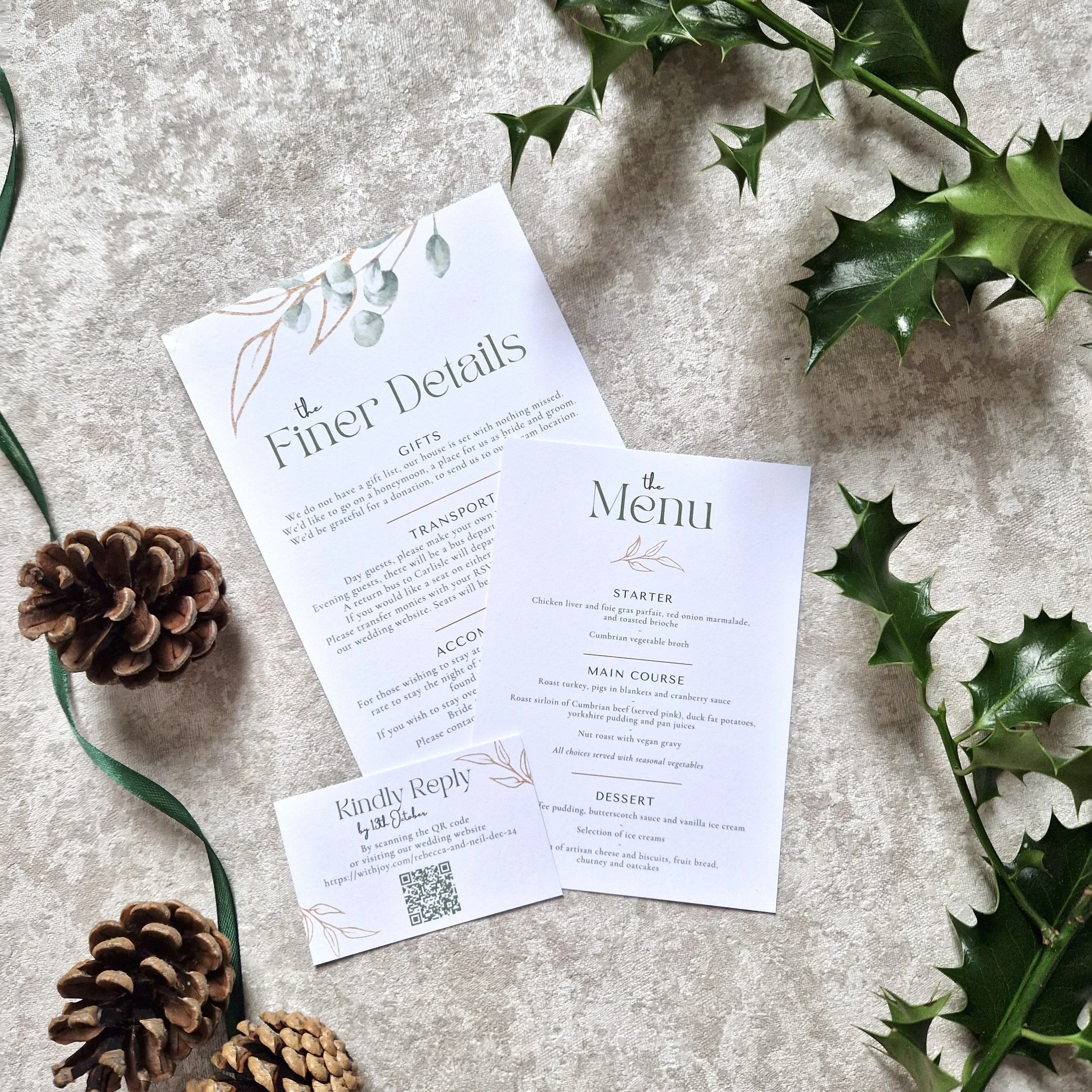 Winter Wedding stationery including a menu and a details card surrounded by pinecones and holly leaves on a textured surface.