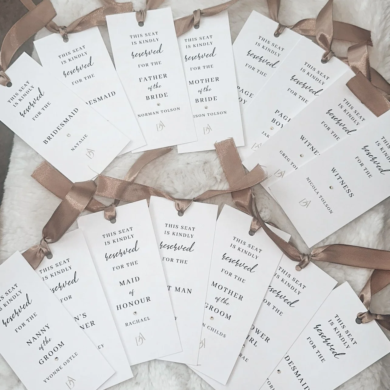 Wedding seat reserved tags for various roles, such as bride, groom, maid of honor, mother of the bride, and witnesses, attached to pink ribbons.