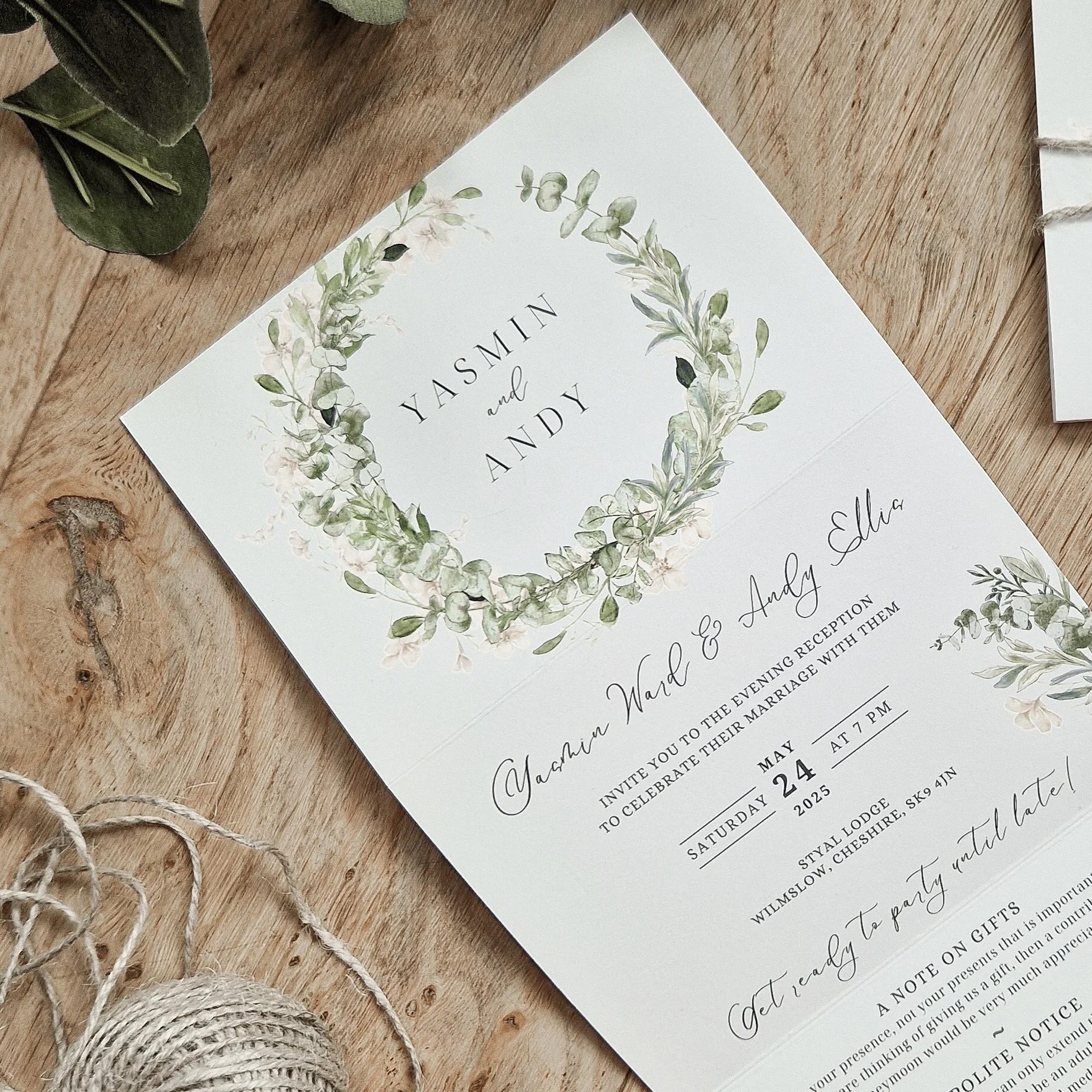 Concertina Wedding invitation card with green floral wreath design, displaying names Yasmin and Andy, and details of the wedding date and location. Styal Lodge Cheshire