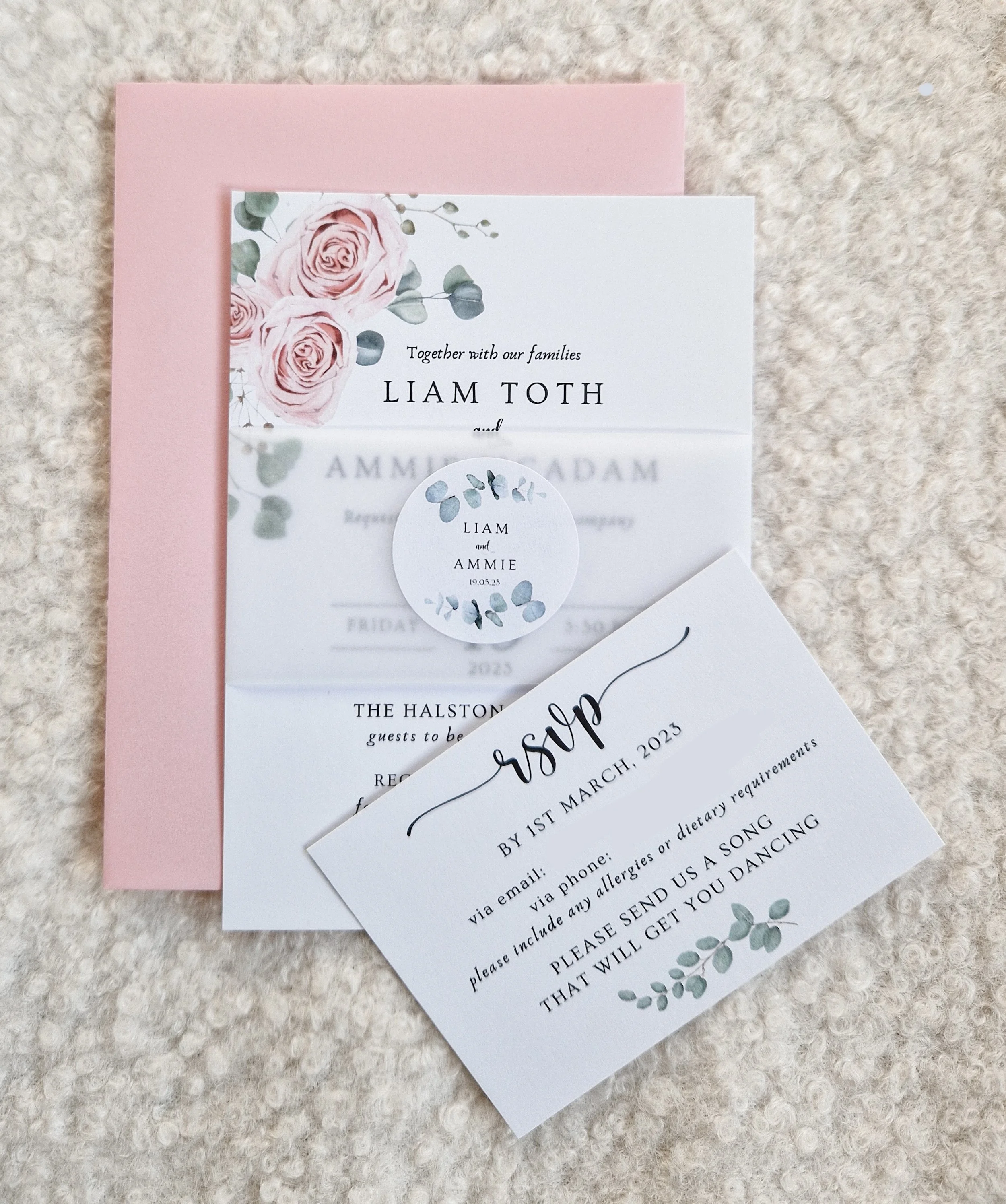 Wedding invitation suite with pink envelope, pink floral rose design, and RSVP card on a textured beige surface. The Halston Carlisle Cumbria