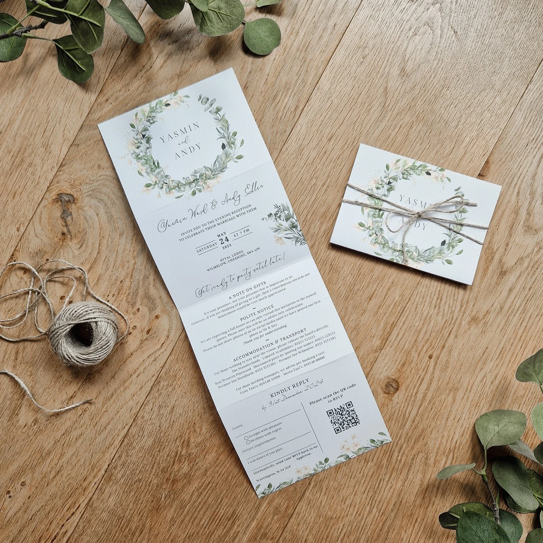 Concertina Wedding invitation for Yasmin and Andy with floral wreath design, placed on a wooden surface with green leaves and a spool of string nearby, and a matching folded card tied with string. Styal Lodge Cheshire
