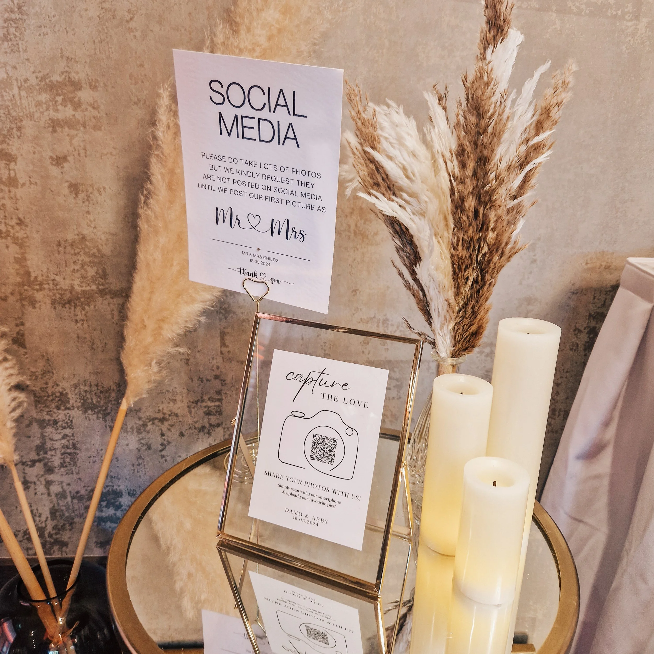 Wedding on the day signage instructing guests about social media photos at a wedding table with candles and dried pampas grass. QR code