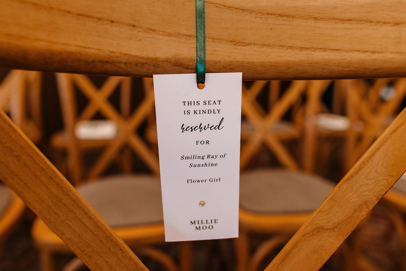 Wedding Seat reservation tag hanging on a wooden chair, with a decorative diamond-shaped embellishment near the bottom.