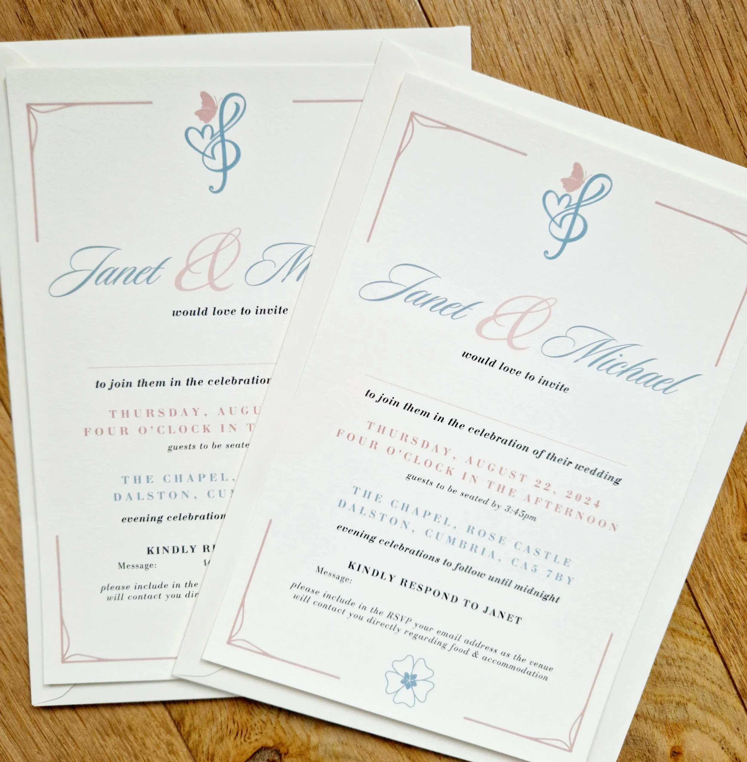 Bespoke wedding invitation cards with decorative borders, floral and heart motifs, and elegant text details placed on a wooden surface. Rose Castle Dalston Carlisle Cumbria. 