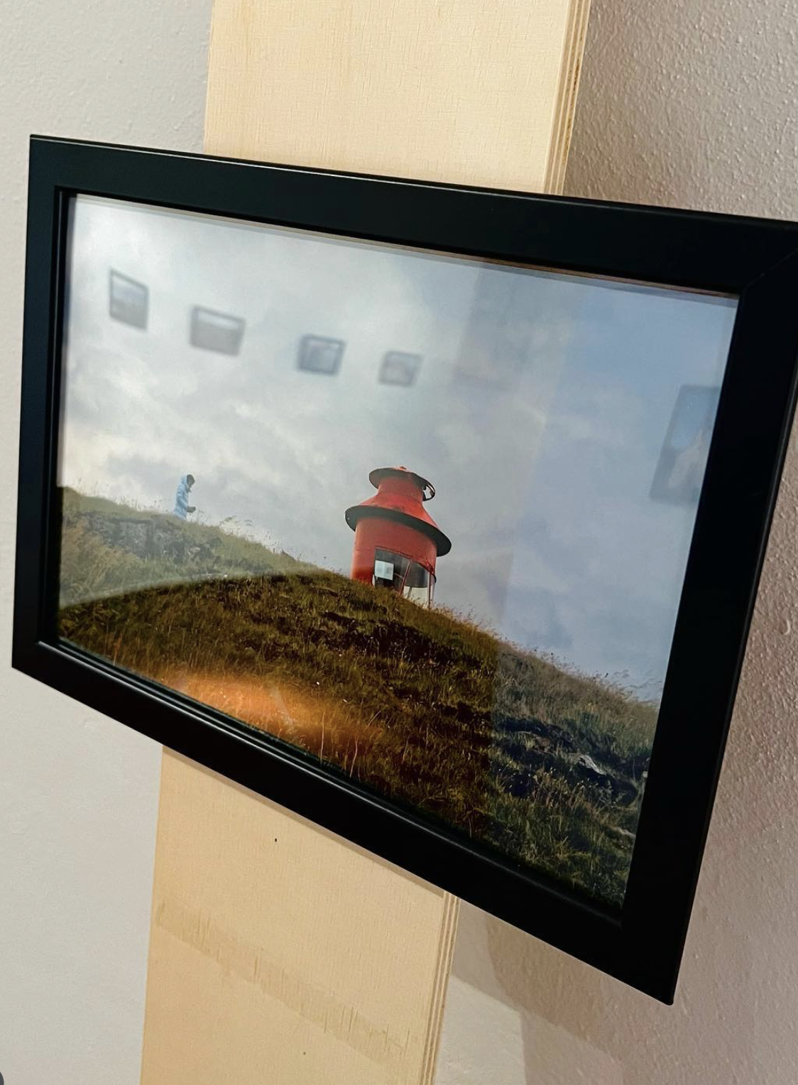 Foto di una cornice con immagine di un faro rosso su una collina verde con nuvole sul cielo.