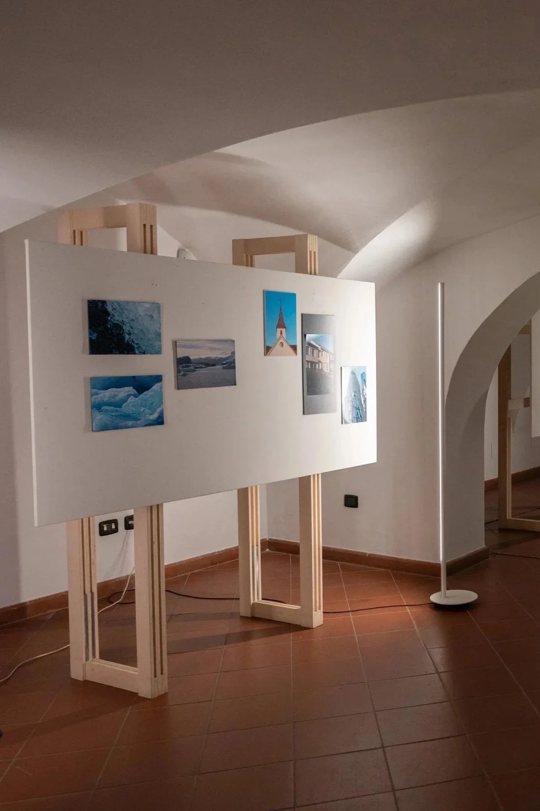 Mostra una parete con diverse fotografie di paesaggi naturali, come montagne, oceani e architetture, con un'illuminazione soffusa in uno spazio espositivo interno.