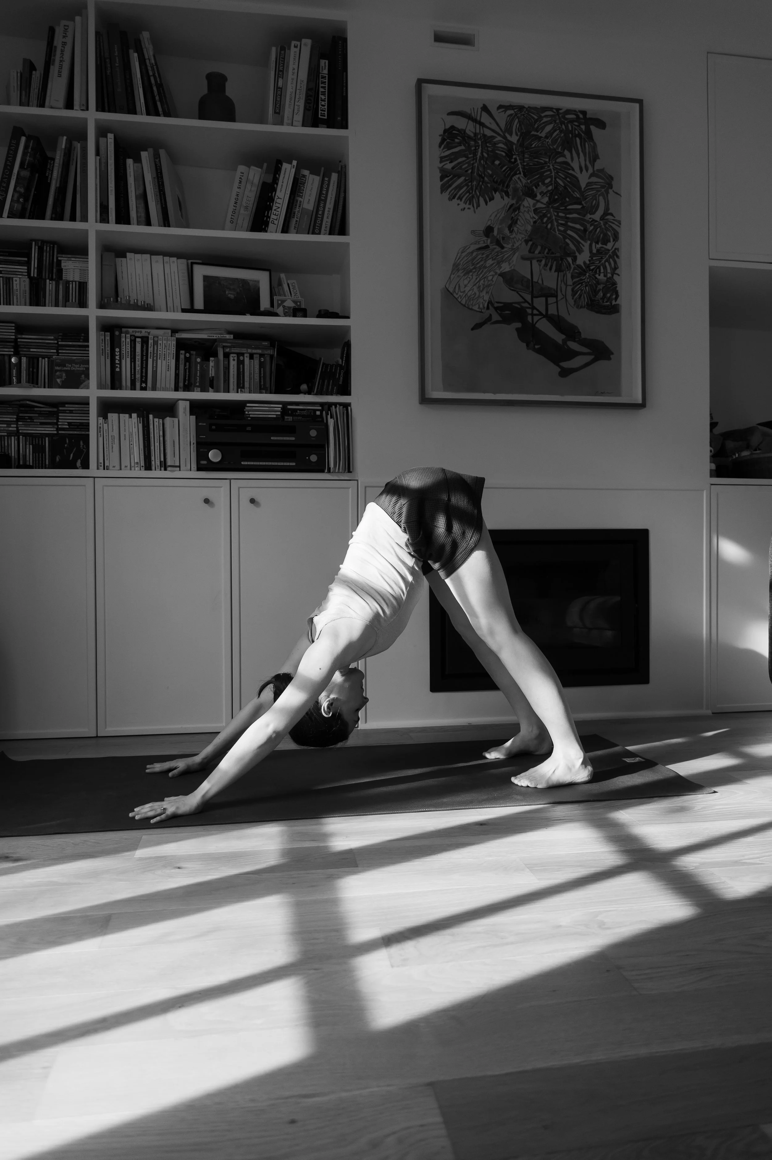 Une personne pratique le yoga dans un salon, en position de chien tête en bas sur un tapis de yoga.