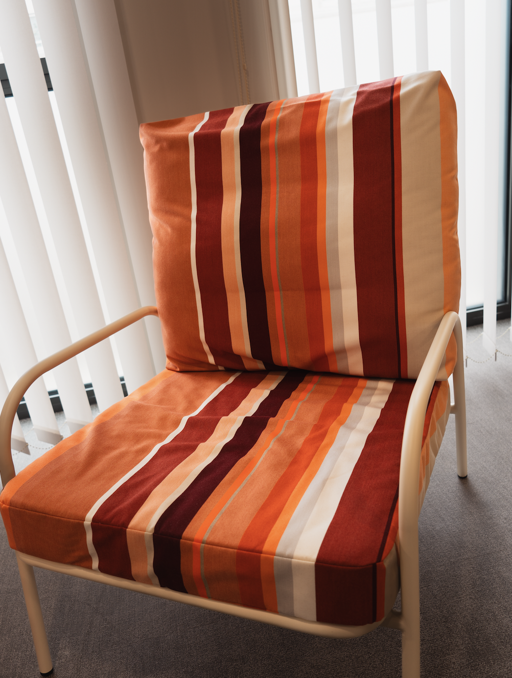 Fauteuil avec un coussin et une housse à motif rayé en couleurs chaudes, placé près de rideaux en voilage blanc.