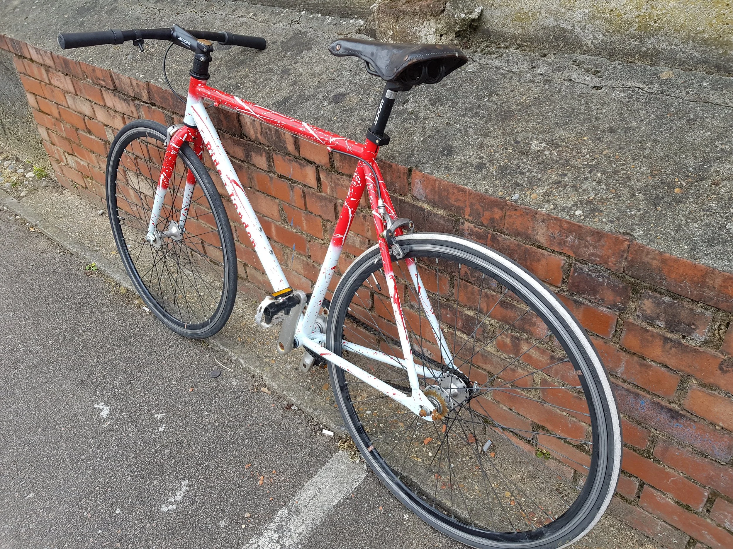 Red and white bicycle leaning against brick and concrete wall on sidewalk.