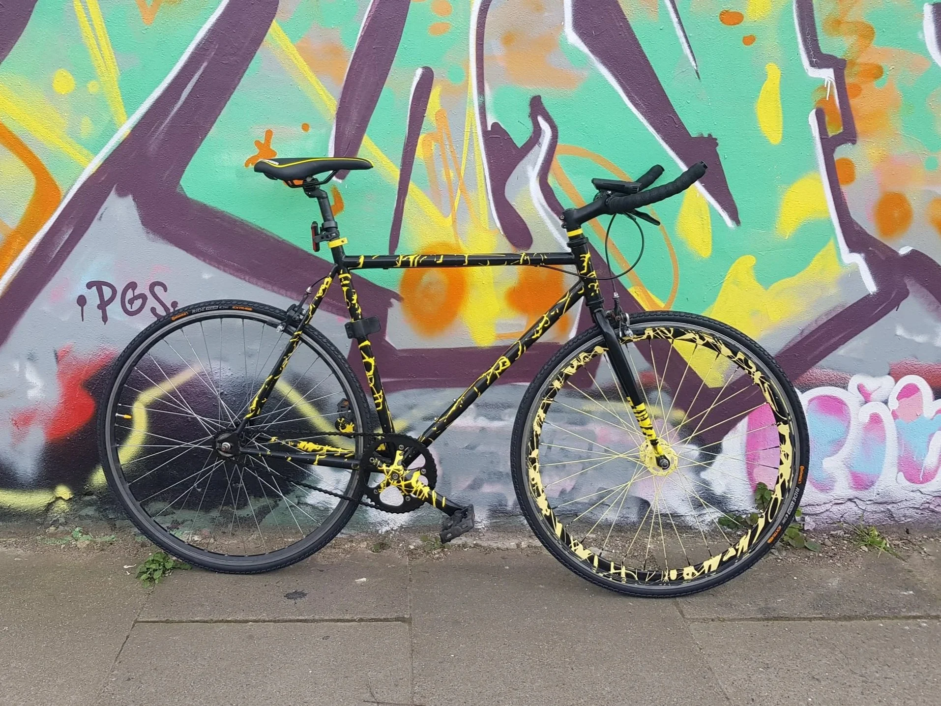 A black and yellow bicycle leaning against a colorful graffiti wall, with our Dribble style