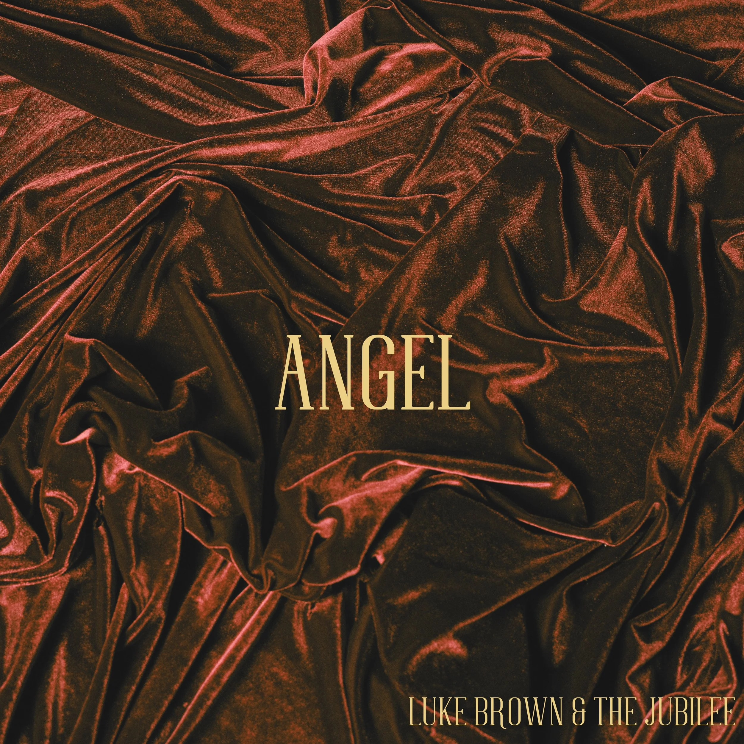 Cover art featuring dark red velvet fabric with the title 'ANGEL' in large beige font centrally placed and the artists 'LUKE BROWN & THE JUBILEE' at the bottom right corner.