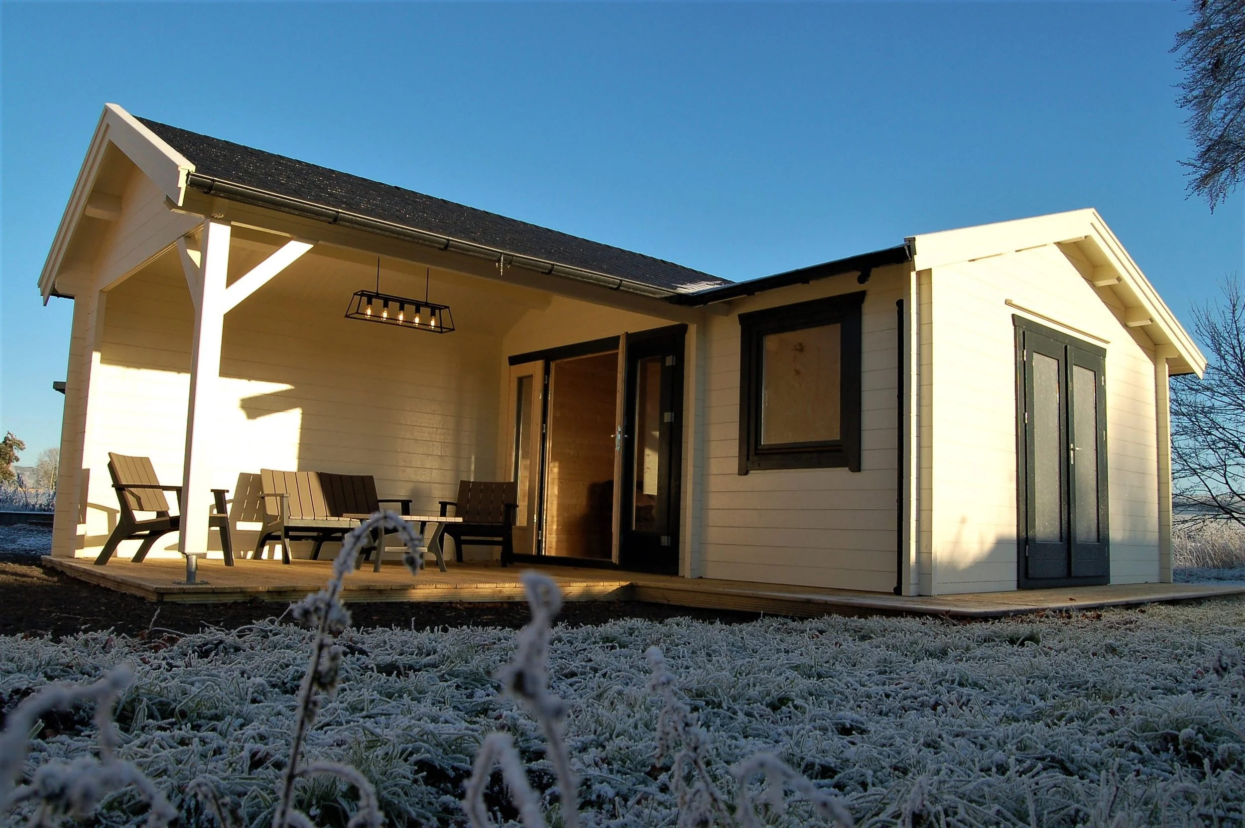 A small, cream-colored house with black trim and a porch, set on a frosty ground with snow-covered grass under a clear blue sky.