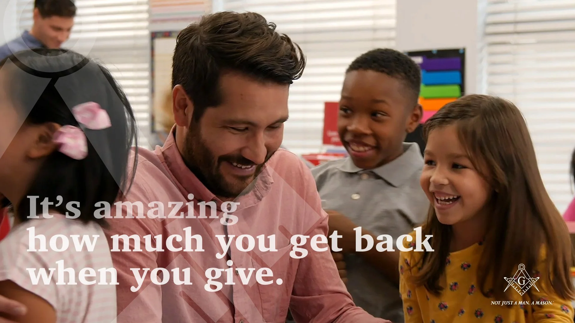 A group of children and an adult smiling and laughing together indoors. The children are of diverse ethnic backgrounds. There is text overlay that reads, 'It’s amazing how much you get back when you give.' At the bottom right, there is a logo with the text 'NOT JUST A MAN. A MASON.'