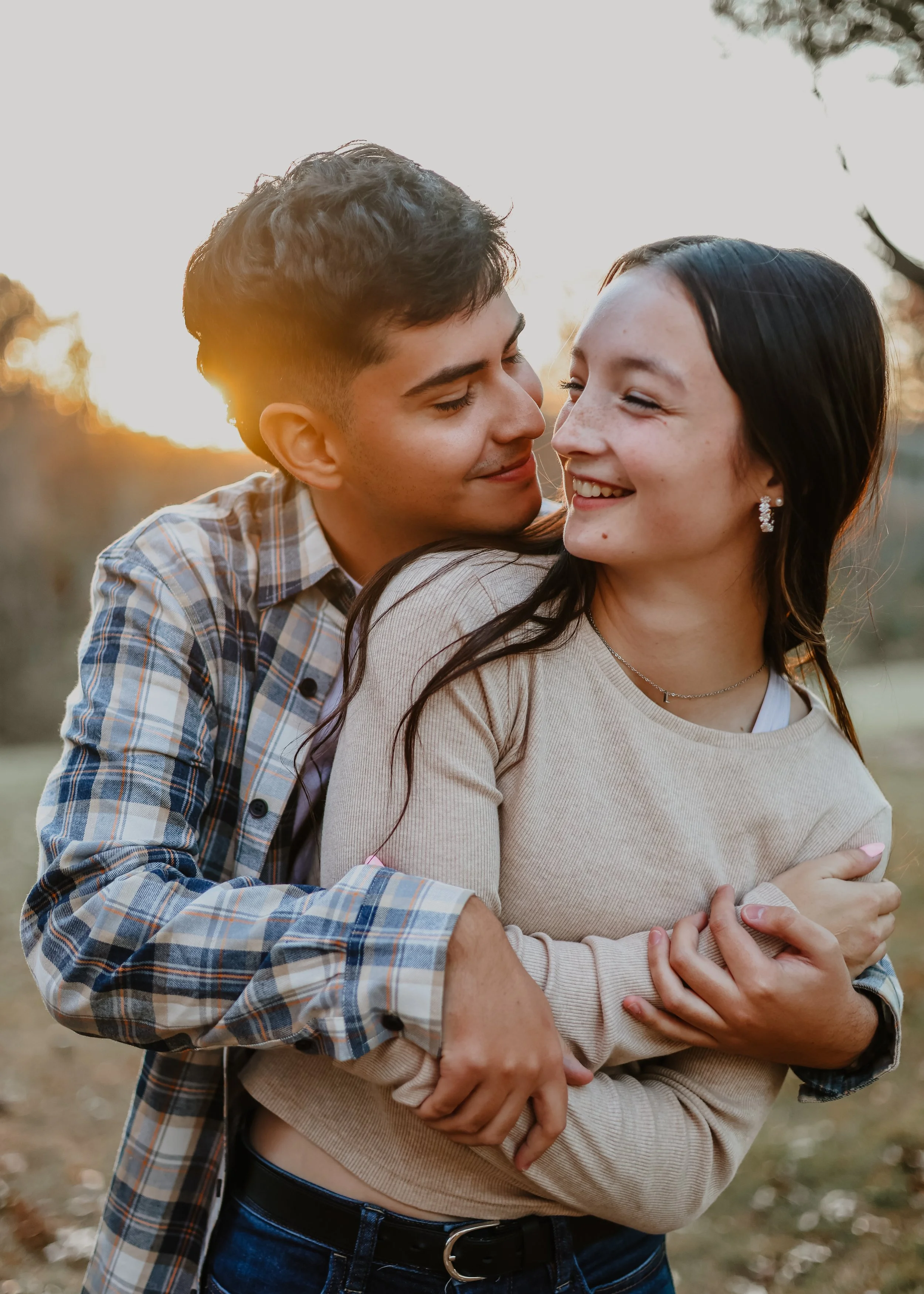 A young couple sharing a joyful moment outdoors at sunset, hugging and smiling at each other.