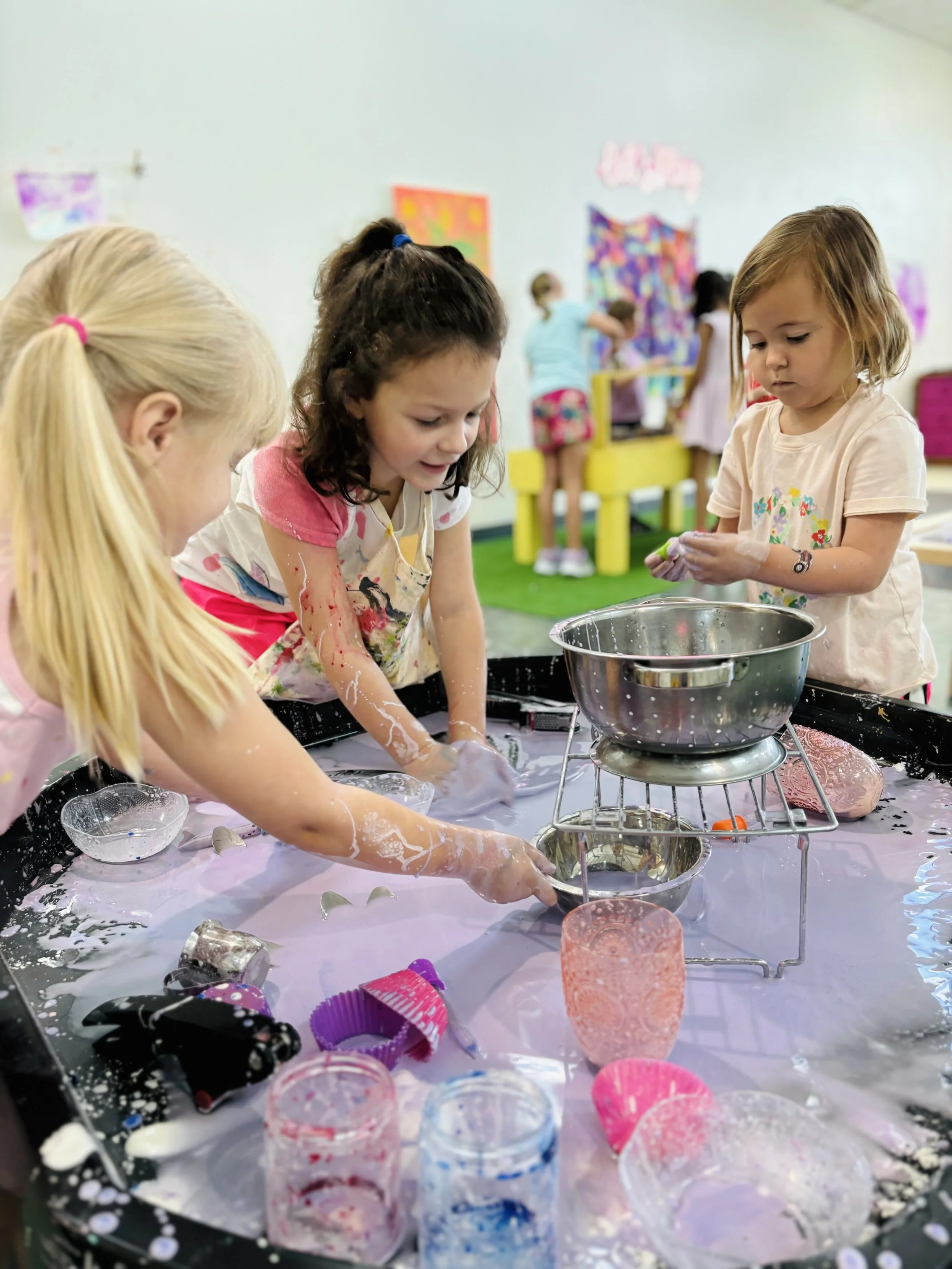 Children playing with slime and toys on a table in a classroom or playroom.