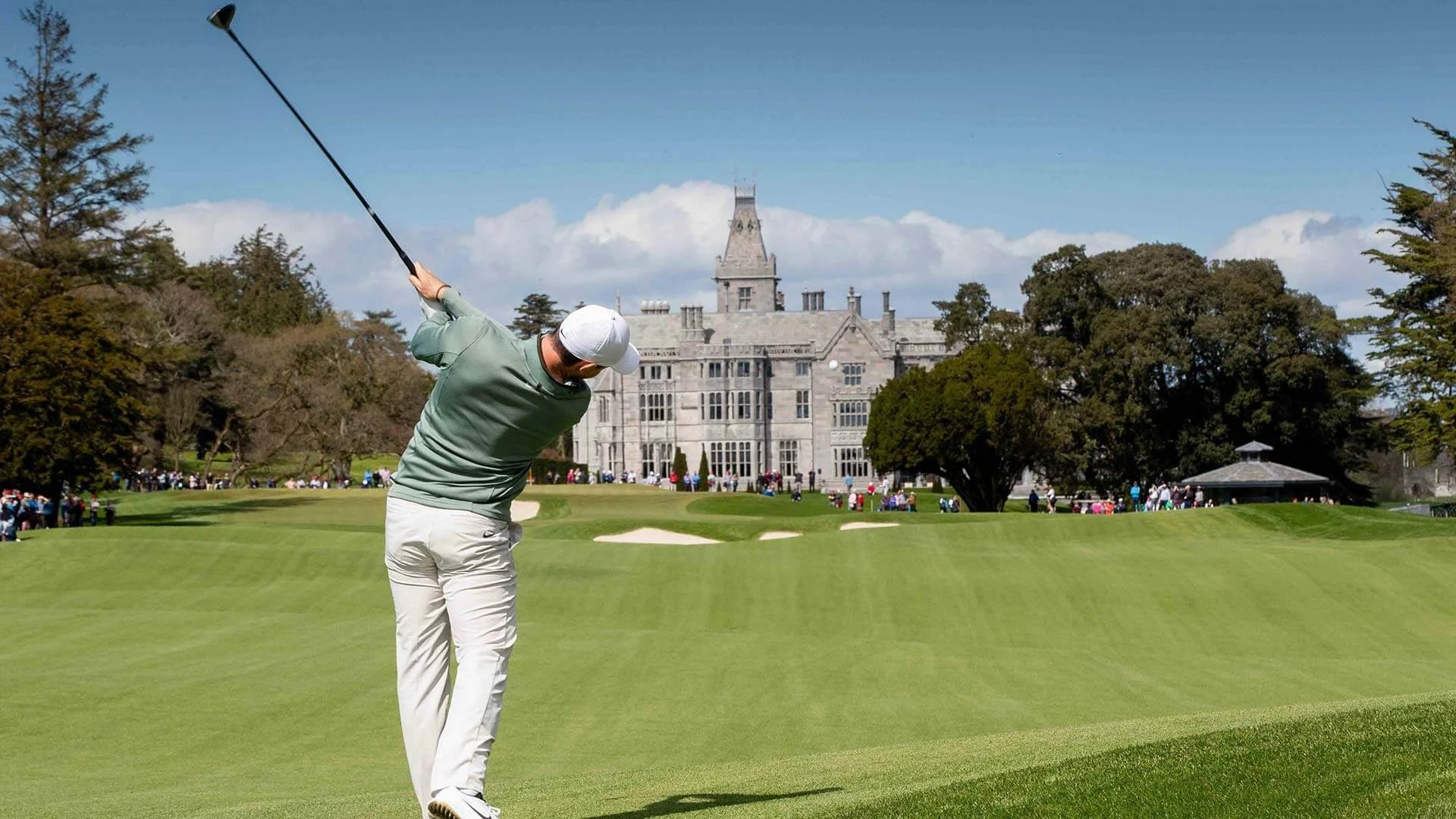 Man swinging golf club on green in front of adare manor