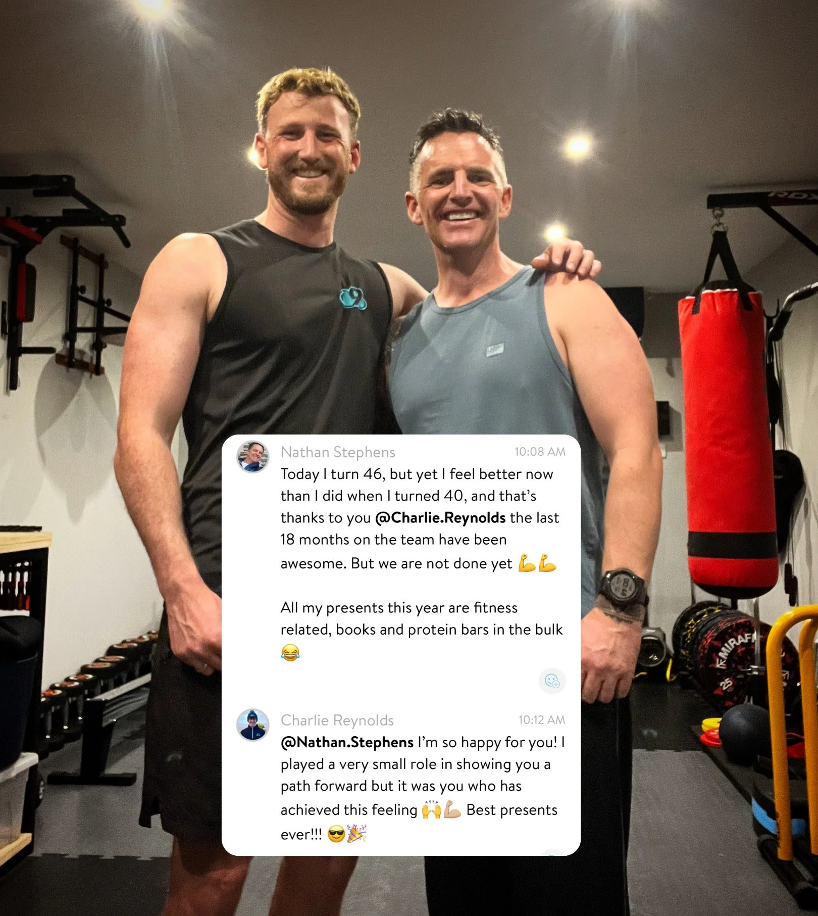 Two men smiling and standing side by side in a gym, with fitness equipment like weights, punching bags, and exercise machines in the background.