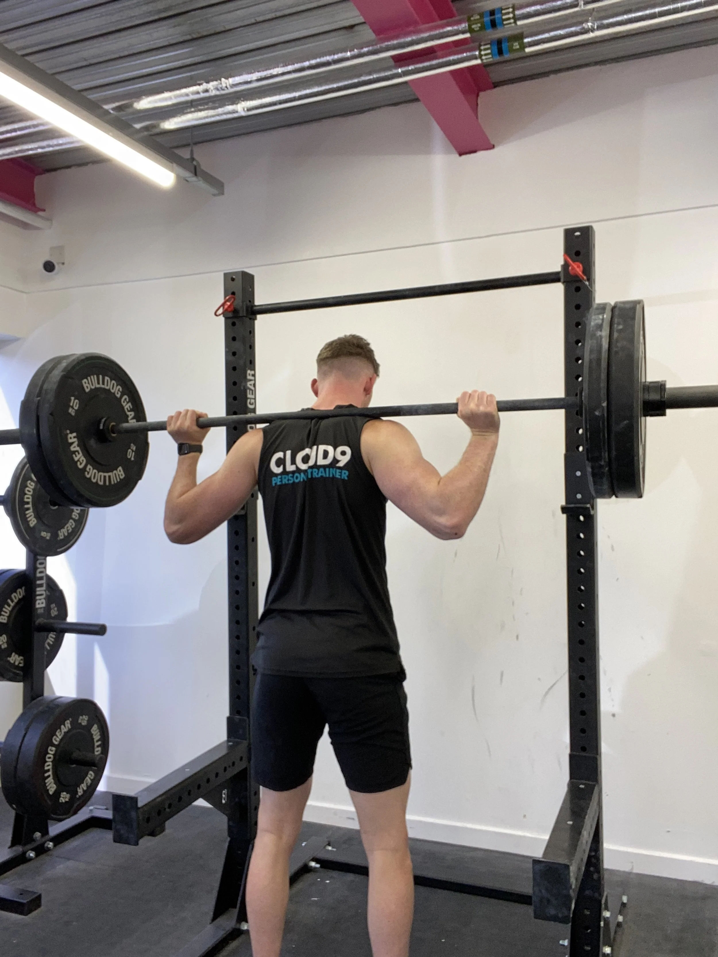 A man performs a squat with a barbell loaded with weights on a squat rack at the gym.