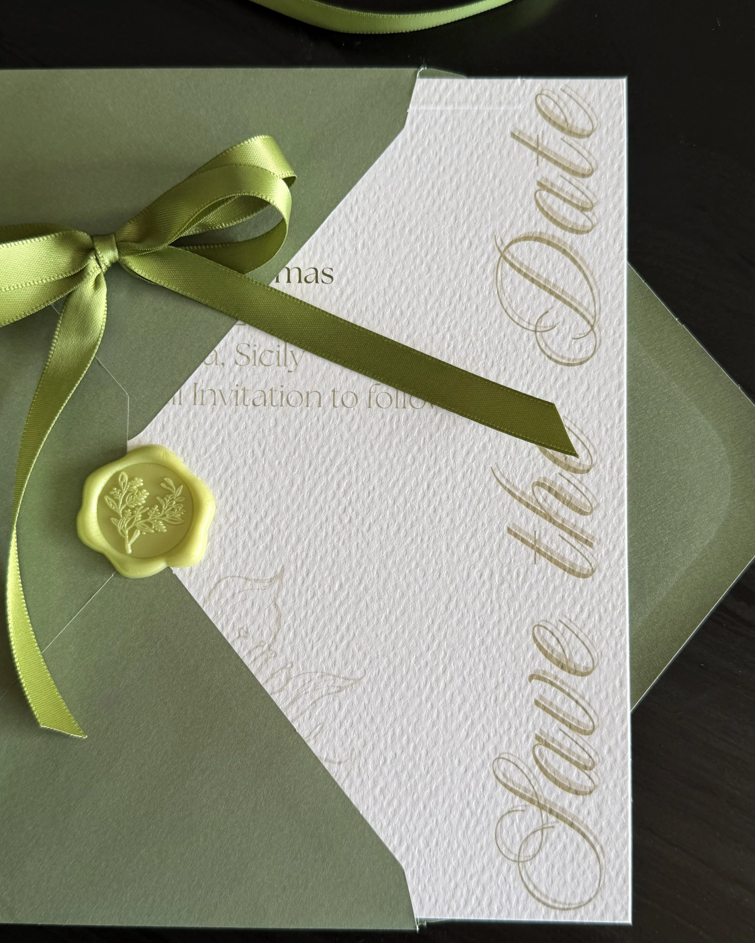 A green gift box with a ribbon, partially opened to reveal a white textured card that reads 'Celebrate Dad' in gold cursive lettering, with a wax seal stamped with a leaf design.