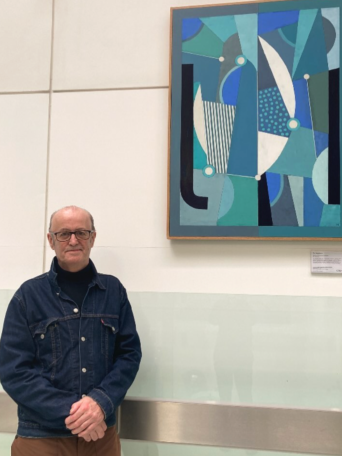 A man standing in front of an abstract geometric painting at an art gallery or museum.