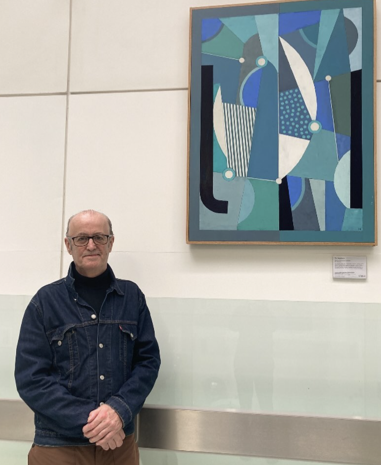 A man standing in front of an abstract blue and green painting in an art gallery.
