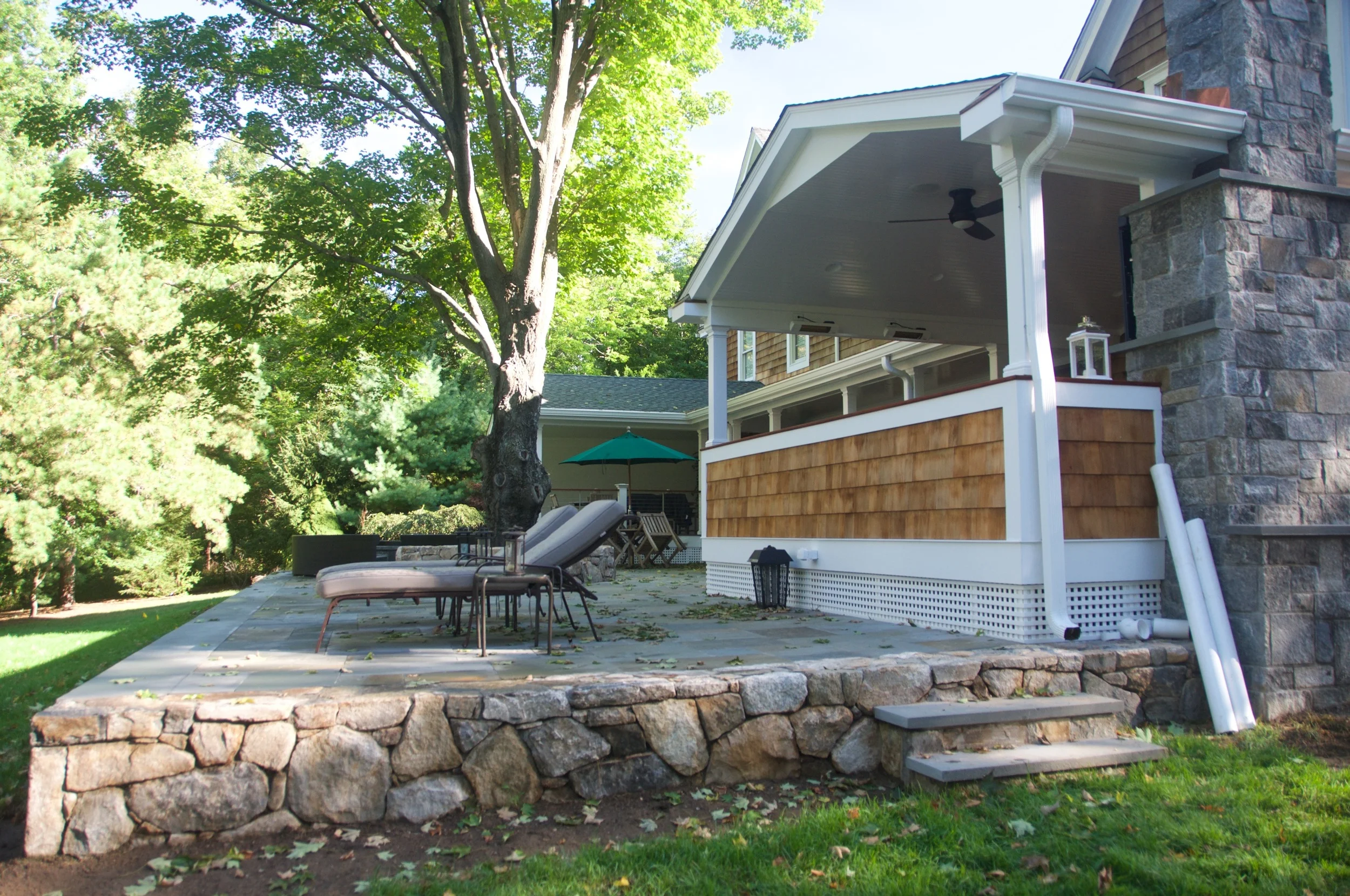 Back porch with stone steps, outdoor seating, and green umbrella, surrounded by trees and lush greenery.
