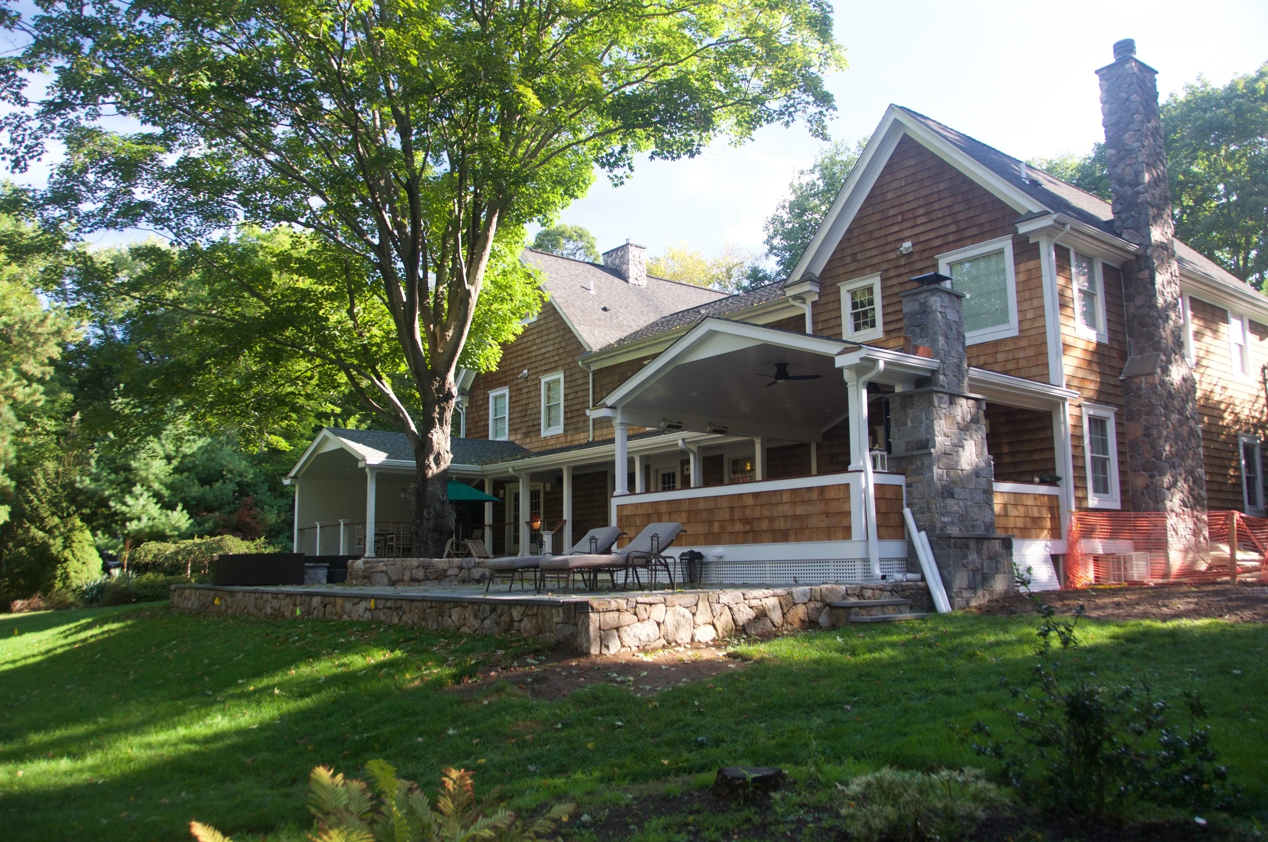 Back view of a two-story house with a large porch, surrounded by trees and a well-maintained lawn.