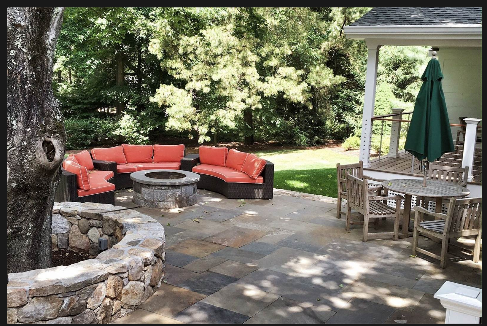 A backyard patio with seating area and fire pit, surrounded by trees and greenery.