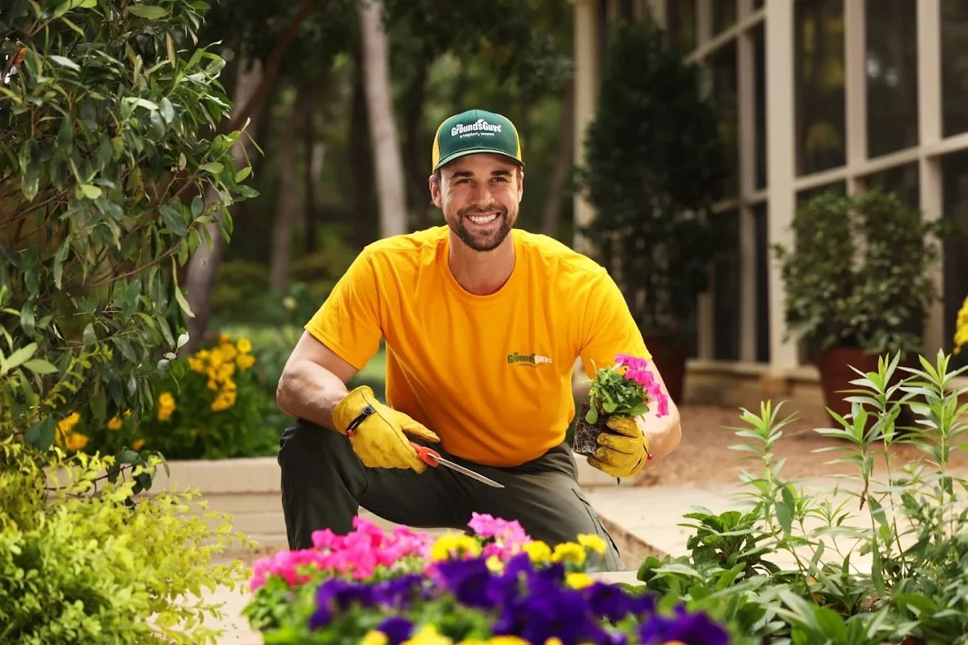 Landscape technician planting seasonal flowers and maintaining a residential garden bed to enhance curb appeal in New Lenox, Illinois.