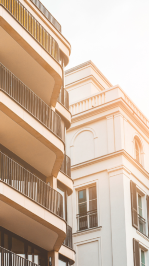 Vue de deux bâtiments modernes avec balcons en fer forgé sous un ciel clair ensoleillé.