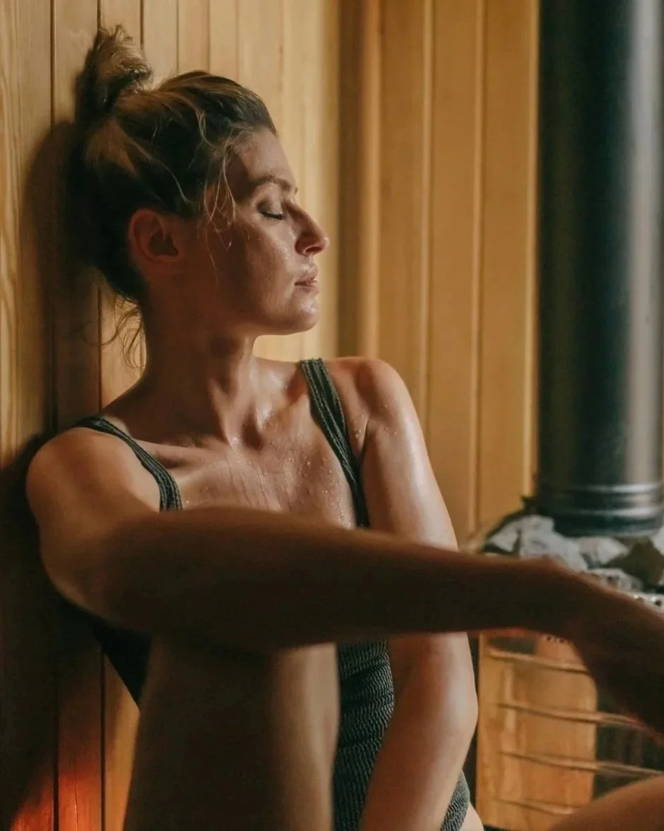 Woman relaxing in sauna, closing eyes, sweating with heat of sauna leaning against wooden panelling of sauna