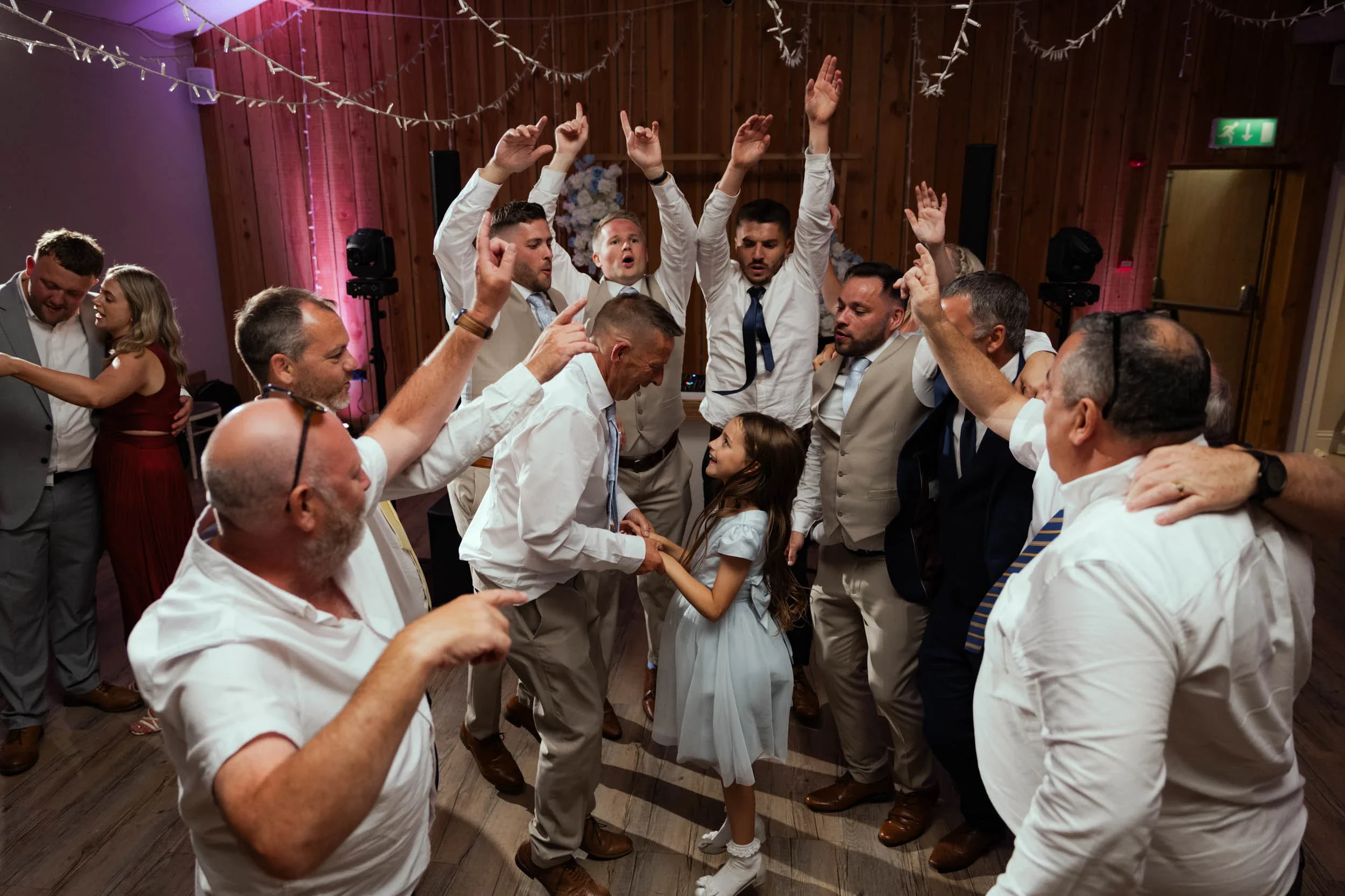 People dancing and celebrating at a wedding reception, with a girl and man holding hands in the center and others surrounding them dancing.