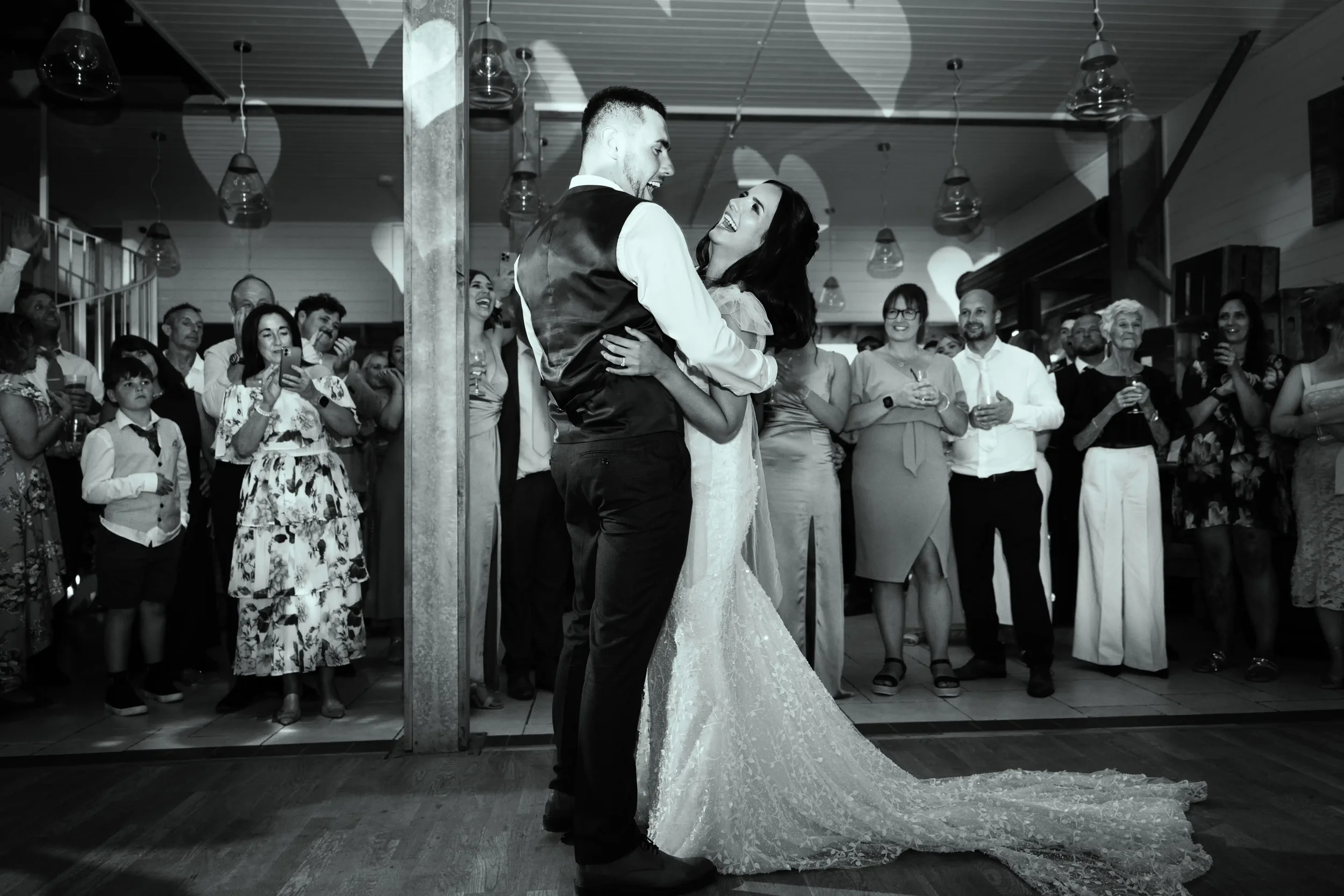 A bride and groom sharing a dance at their wedding reception, surrounded by guests watching and taking photos.