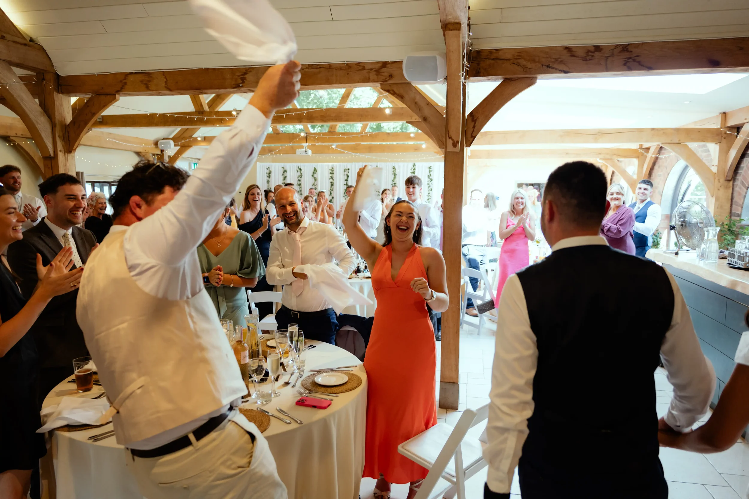 People smiling and celebrating at a wedding reception in a decorated wooden venue.