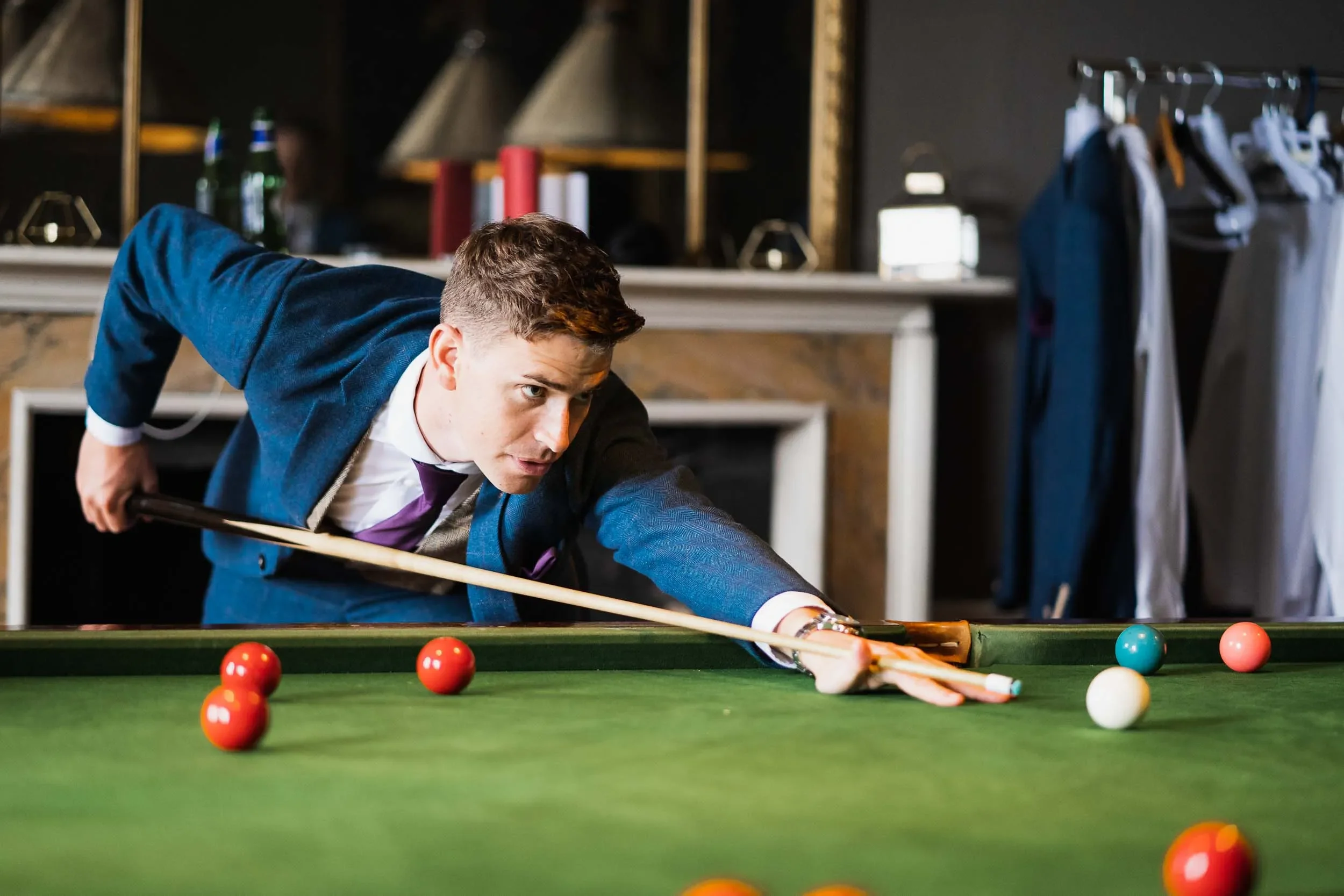 Young man in a suit playing pool on a green table indoors.