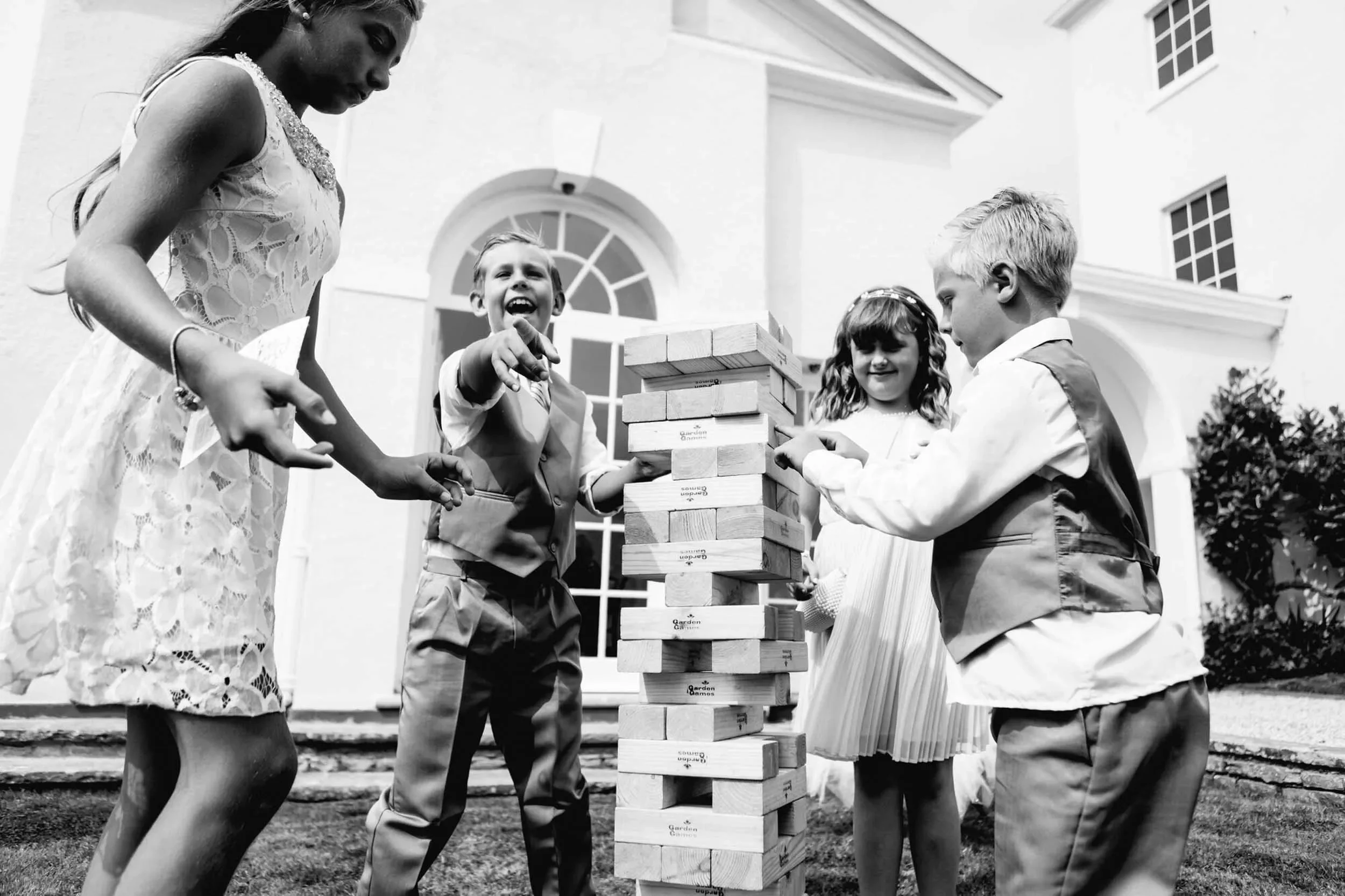 Children and a woman playing giant Jenga outside a house in black and white
