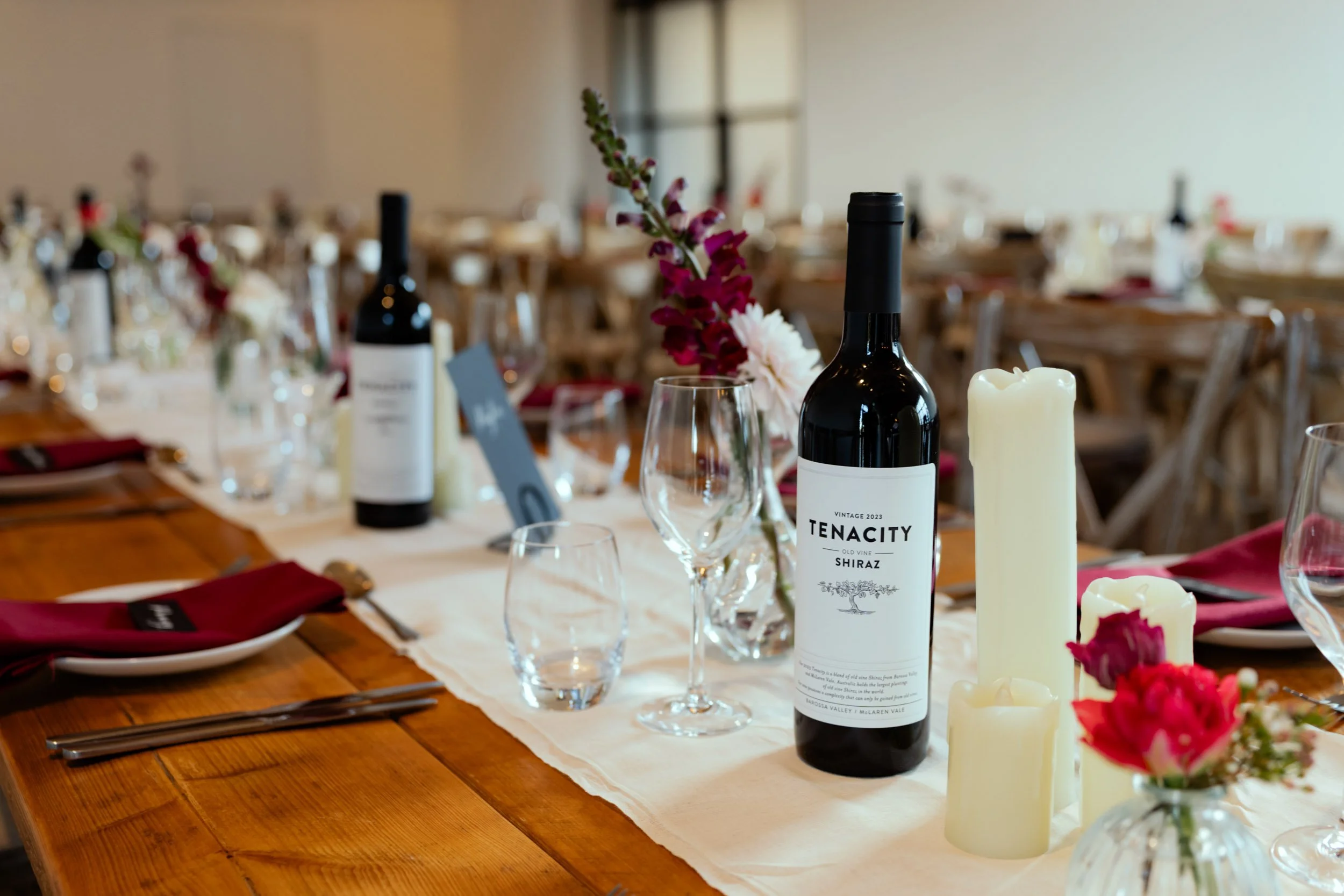 Elegant dining table set with wine bottles, candles, floral arrangements, water glasses, and utensils, ready for a celebration or gathering.