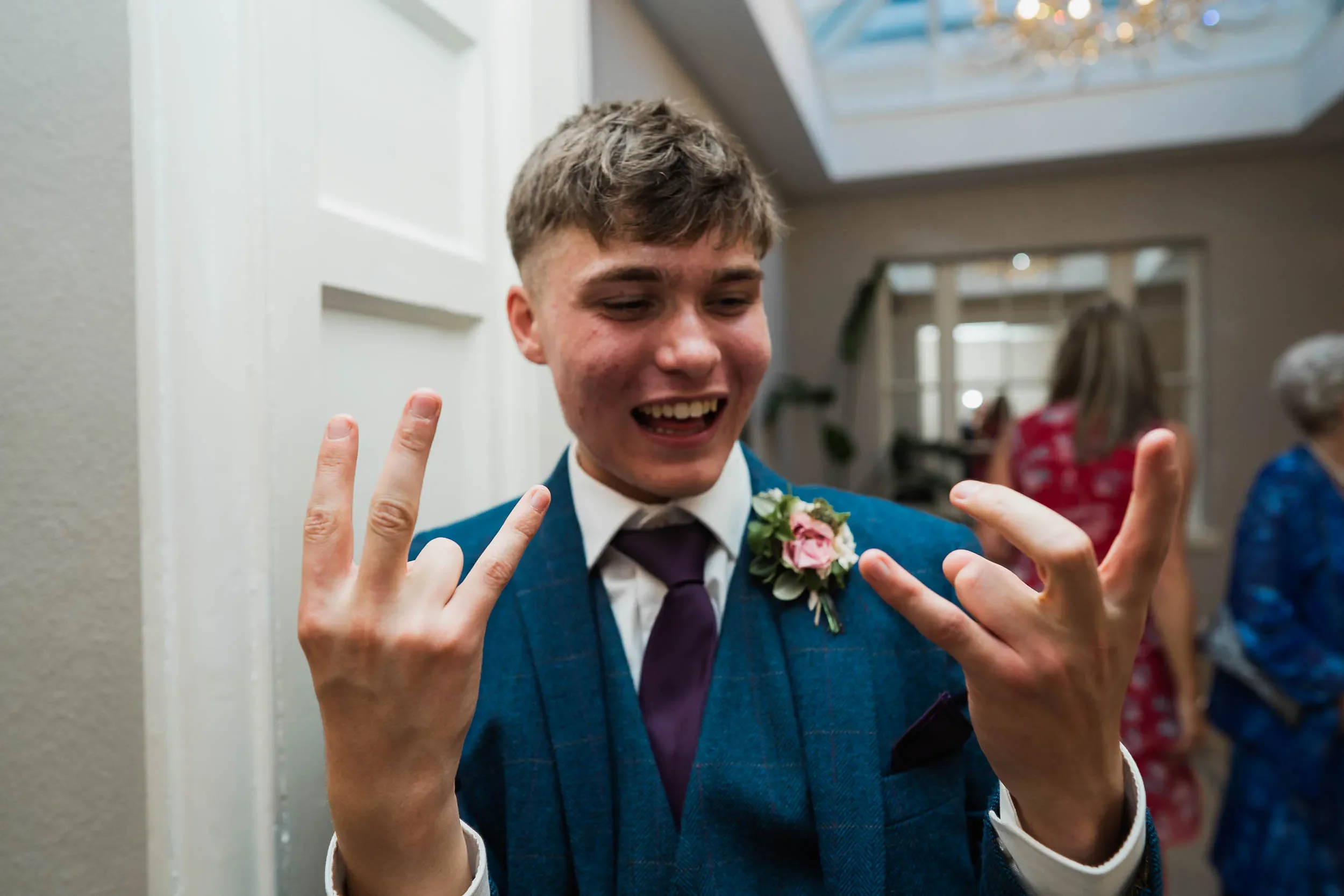 Young man in a blue suit making rock and roll hand gestures at a social gathering.