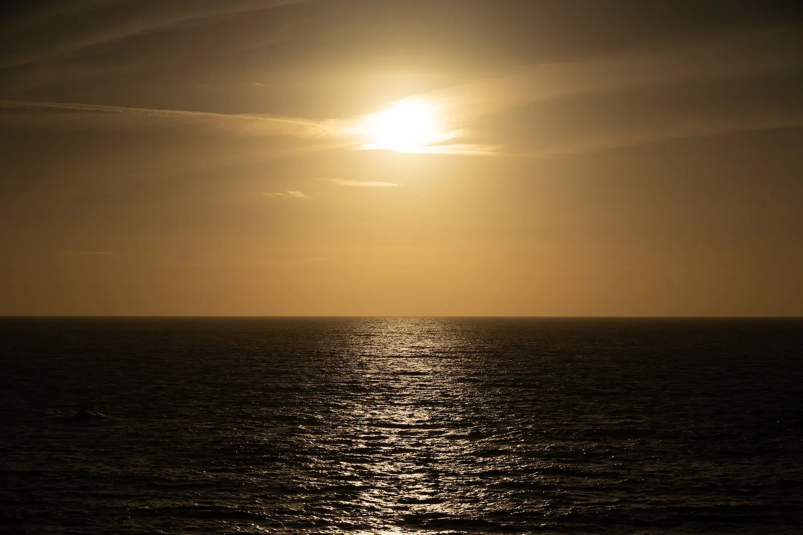 Sunset over the ocean with a reflection on the water and a partly cloudy sky.