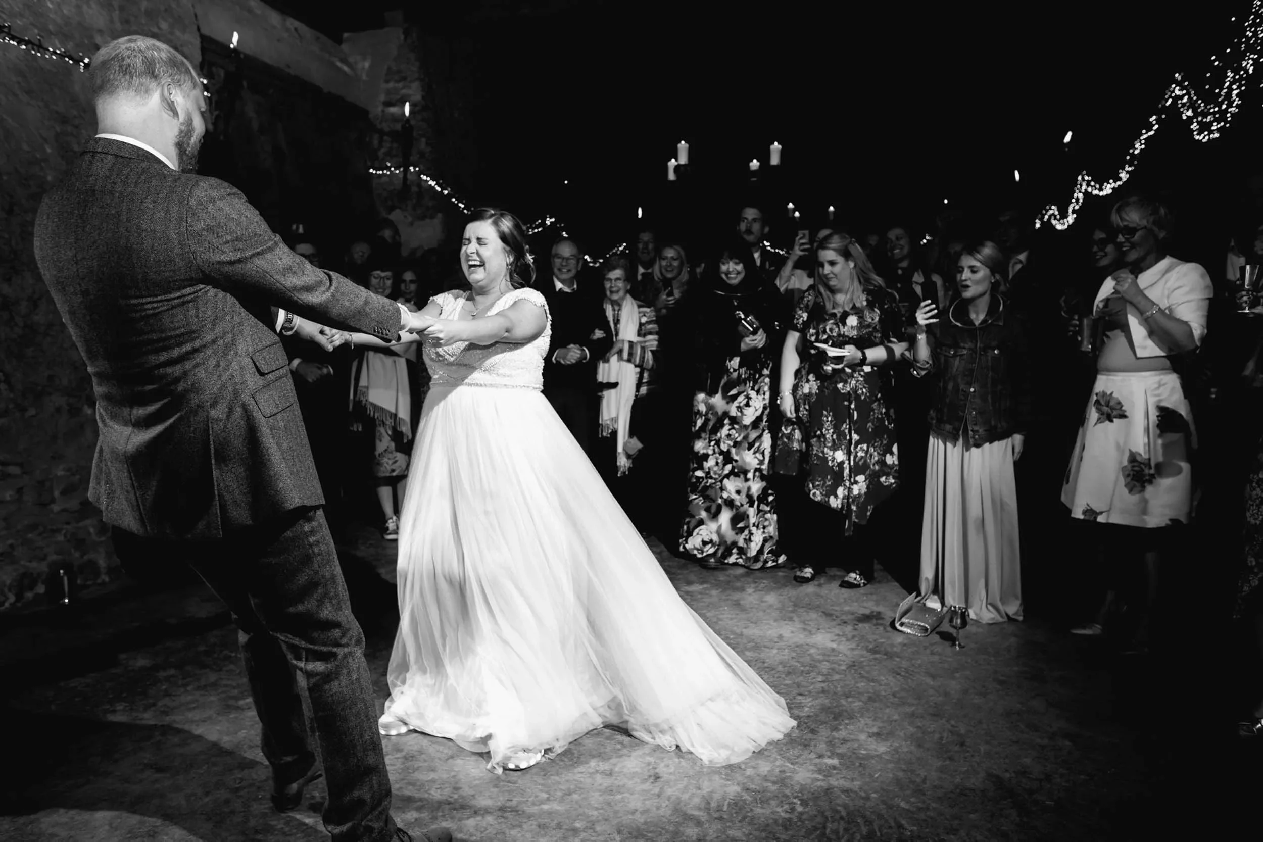 Bride and groom dancing at their wedding reception, surrounded by friends and family in a decorated indoor venue.
