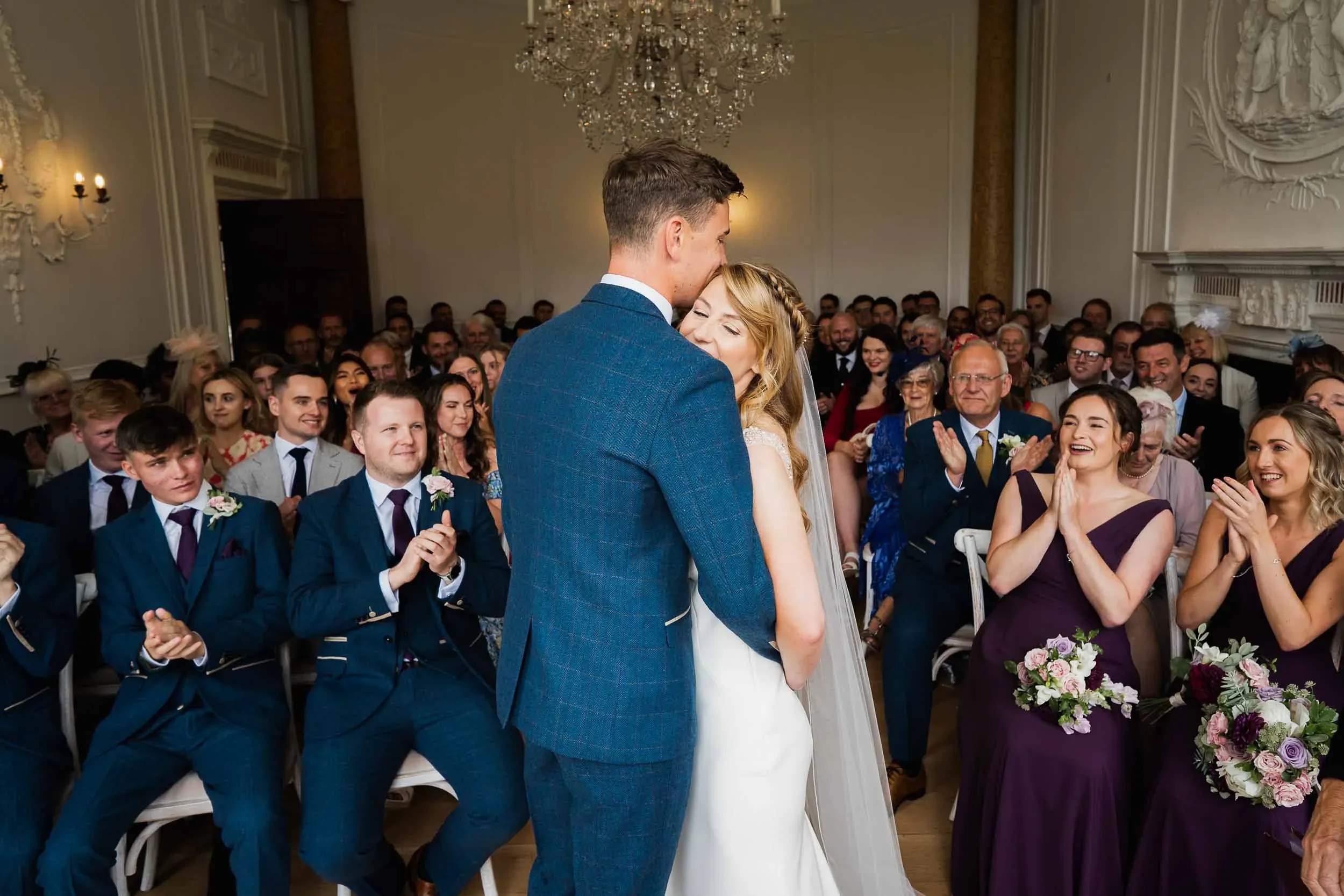 A couple getting married in a wedding ceremony with guests clapping and smiling in a decorated indoor venue.