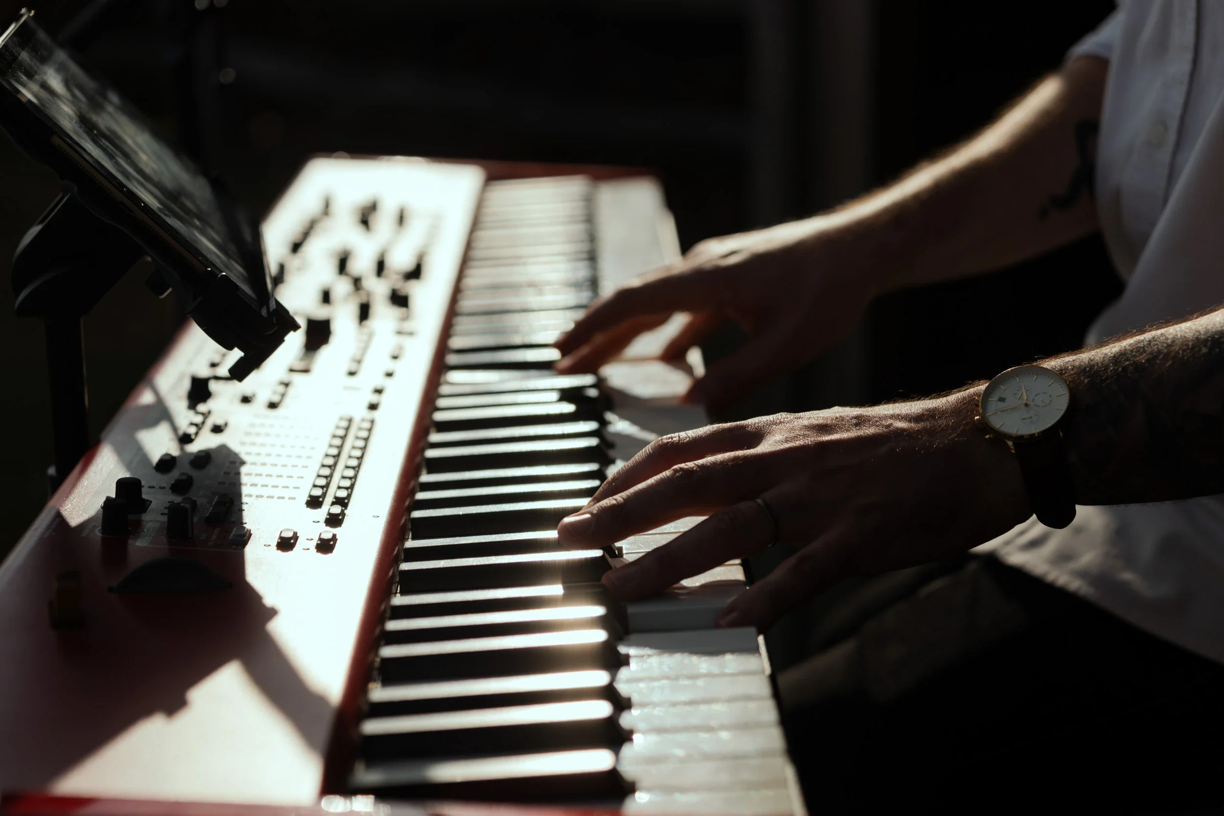 Person playing a red digital keyboard with a watch on their wrist during daylight.
