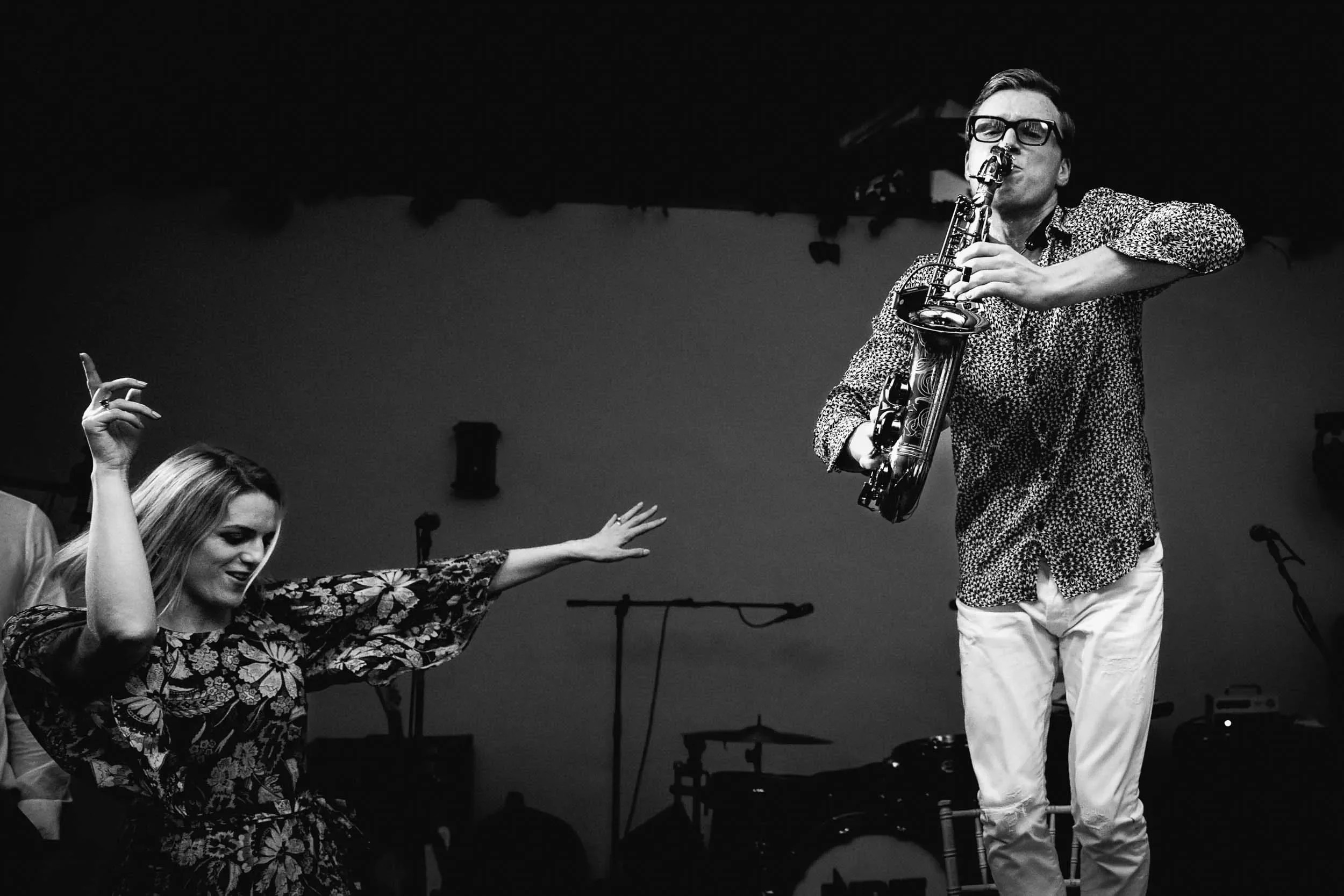 A man playing an alto saxophone on stage while a woman dances in front of him.