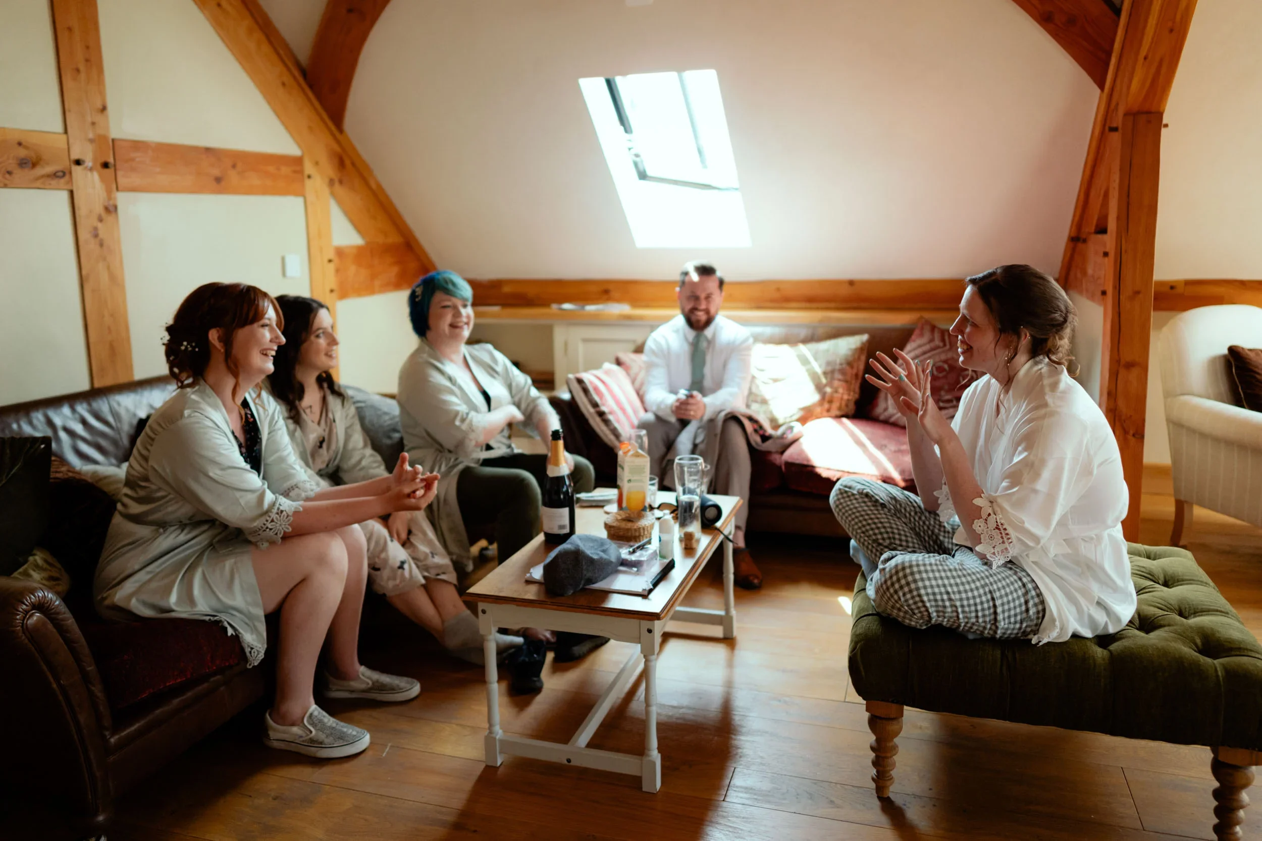 Group of friends sitting in a cozy attic living room, laughing and chatting, with a coffee table holding drinks and snacks.